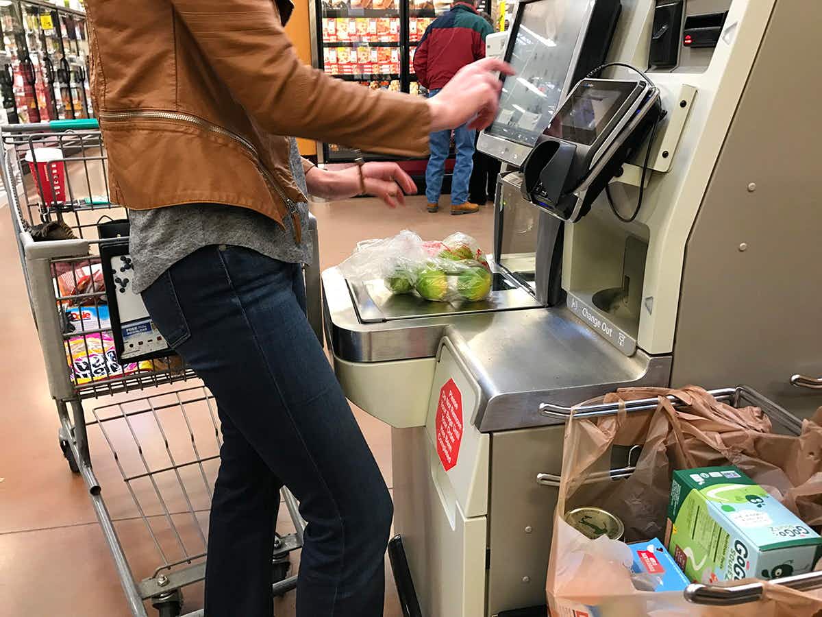 A woman using self checkout at a grocery store.