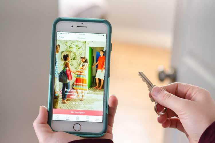 Person holding a key after unlocking a room door with a phone open to the airbnb app in the other hand.