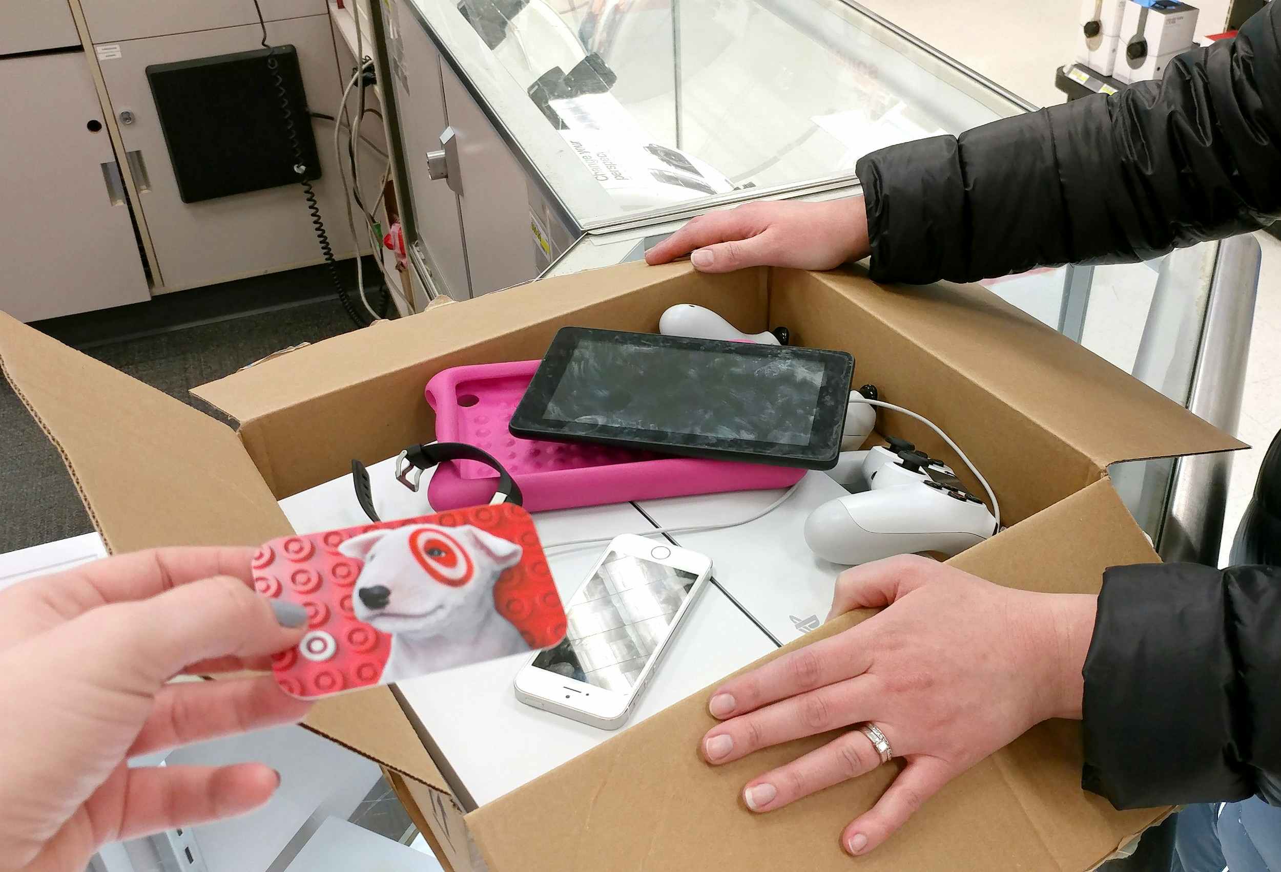 A person setting a box of used electronics on a counter at Target and another person handing them a Target gift card.