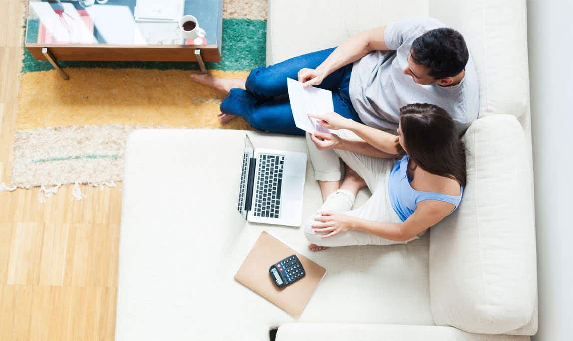 man and woman on couch with laptop, calculator, and paperwork