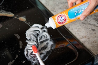 Arm & Hammer toothpaste being applied to a stove with a tooth brush
