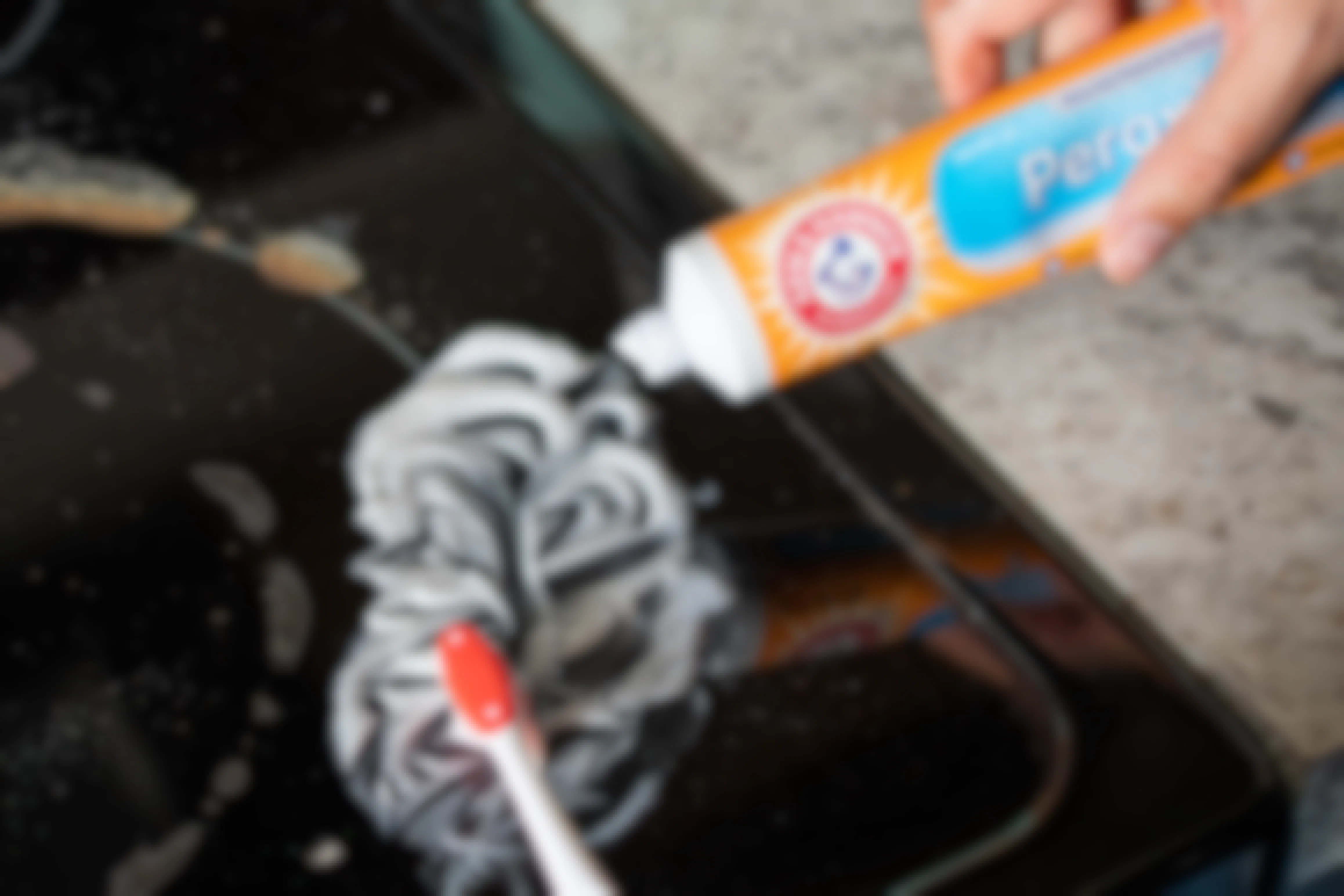 Arm & Hammer toothpaste being applied to a stove with a tooth brush