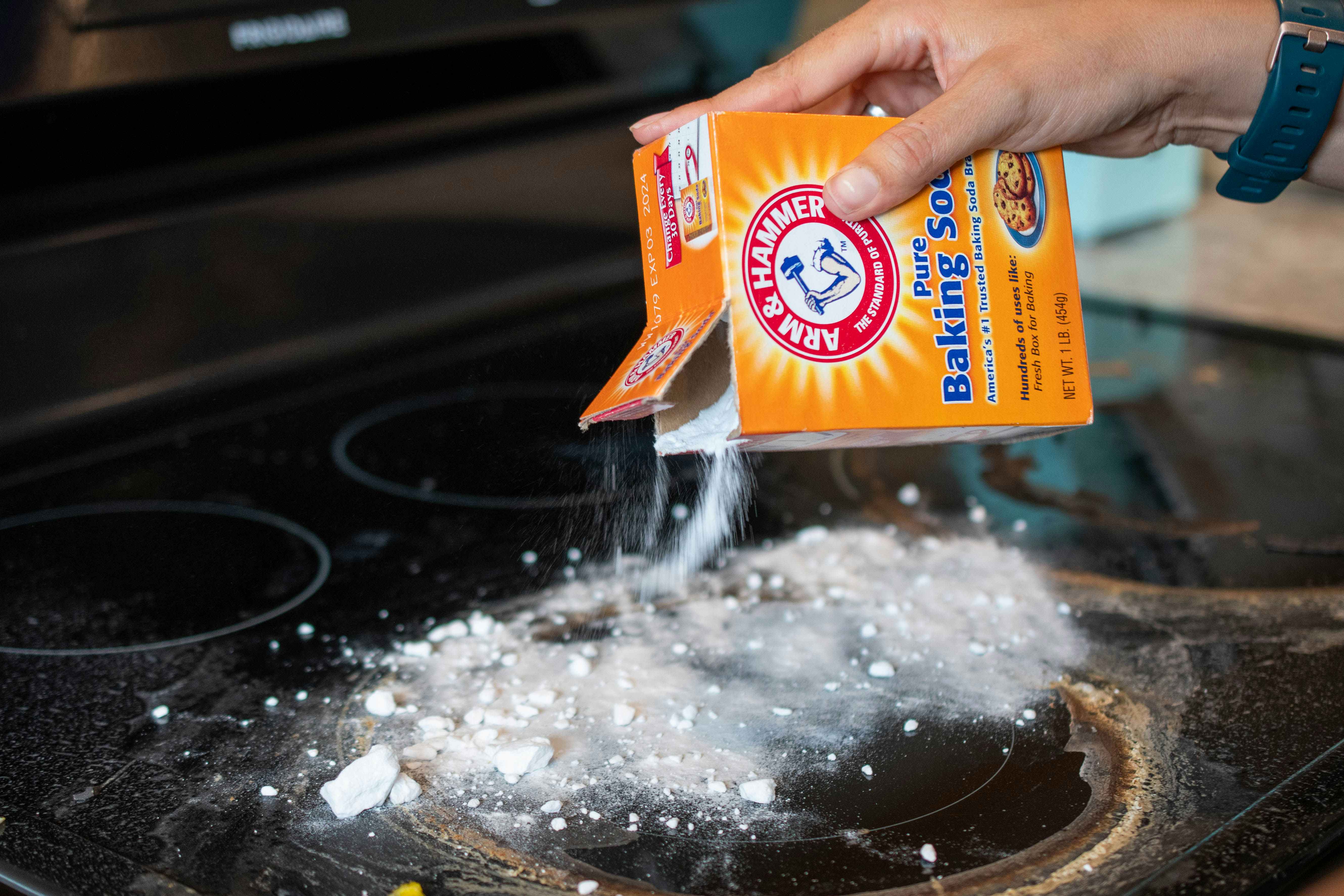 A person sprinkling baking soda onto a stove