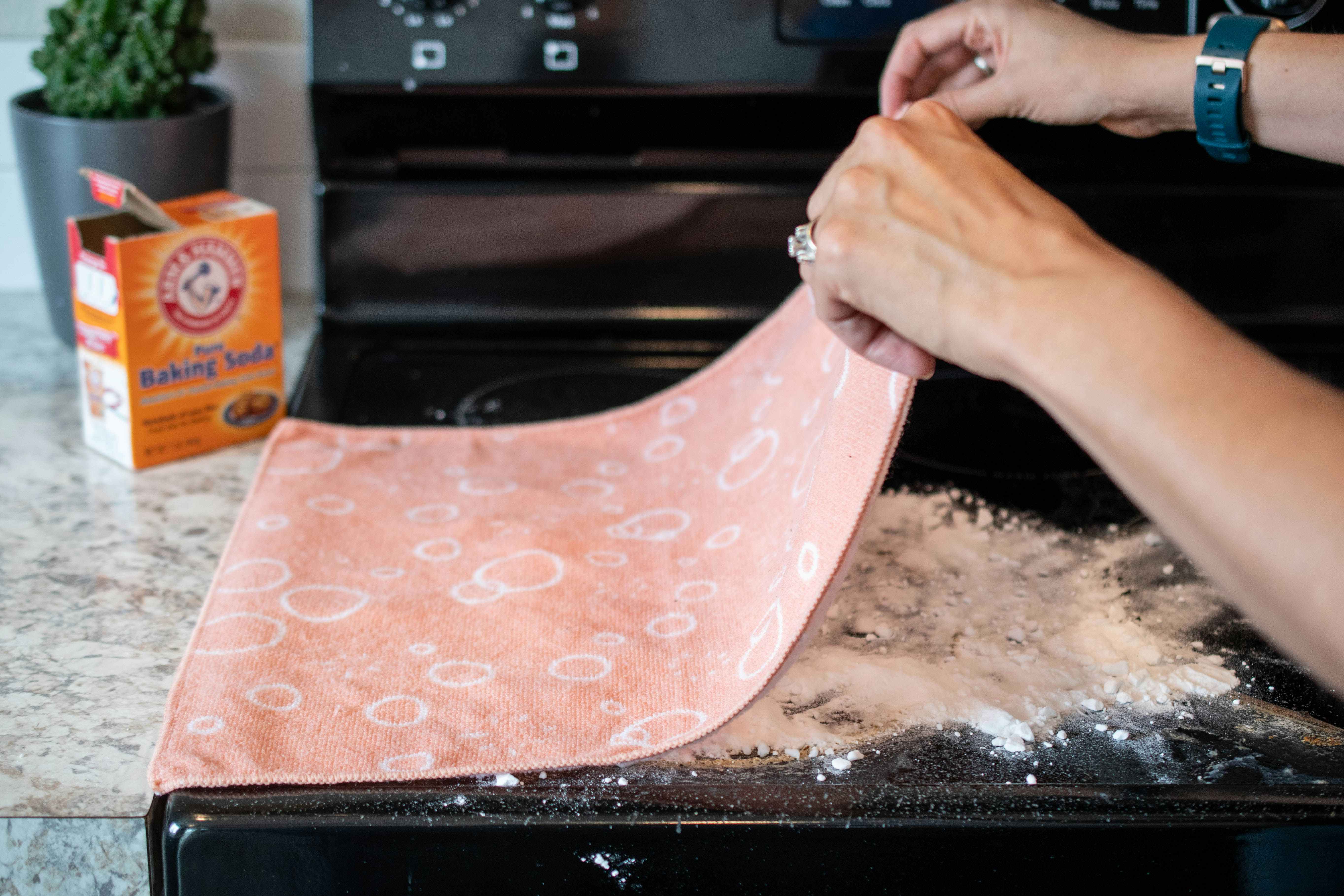 A person laying a peach colored towel over a stove top covered in baking soda