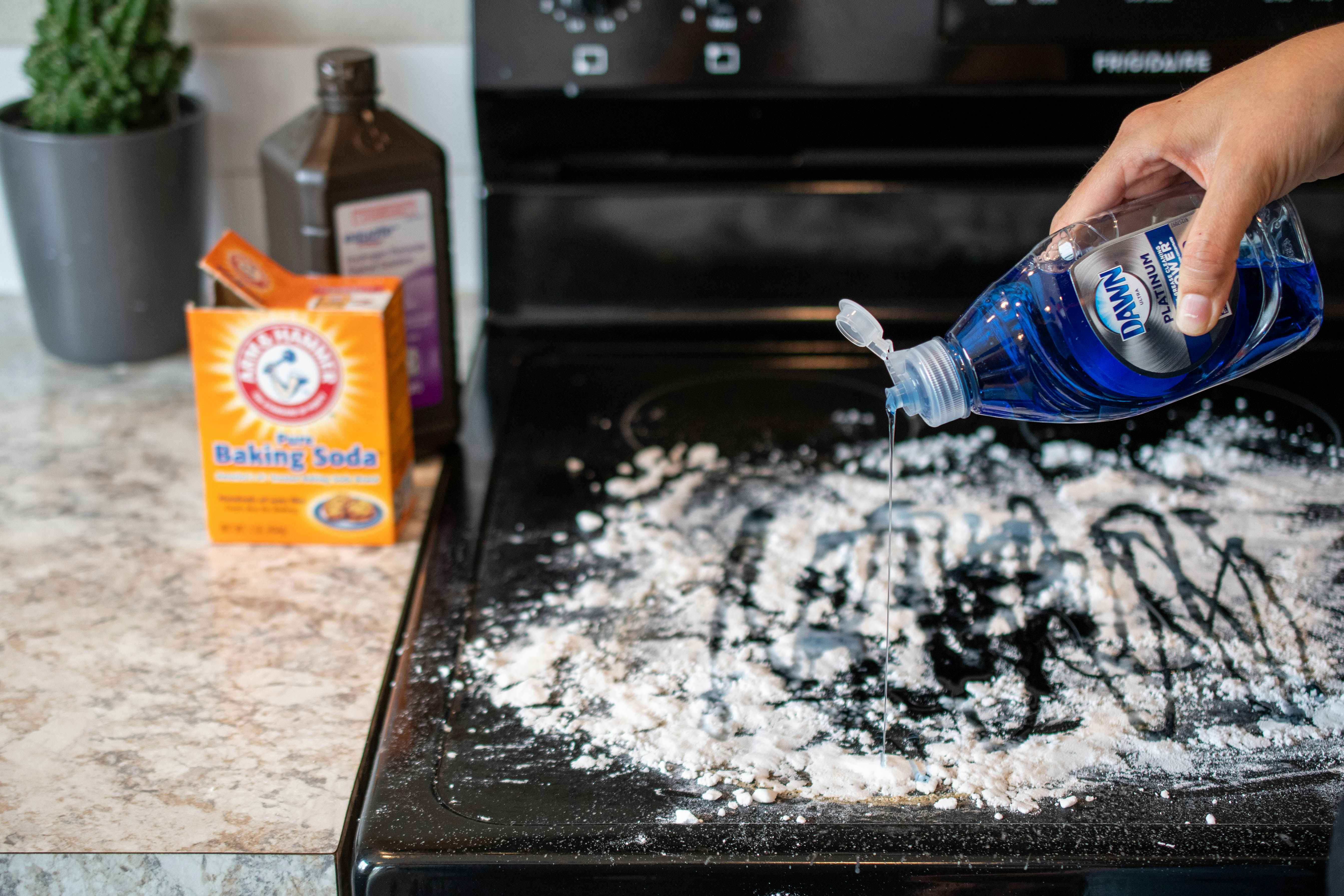 A person drizzling dawn dish soap on top of a stove covered in baking soda.