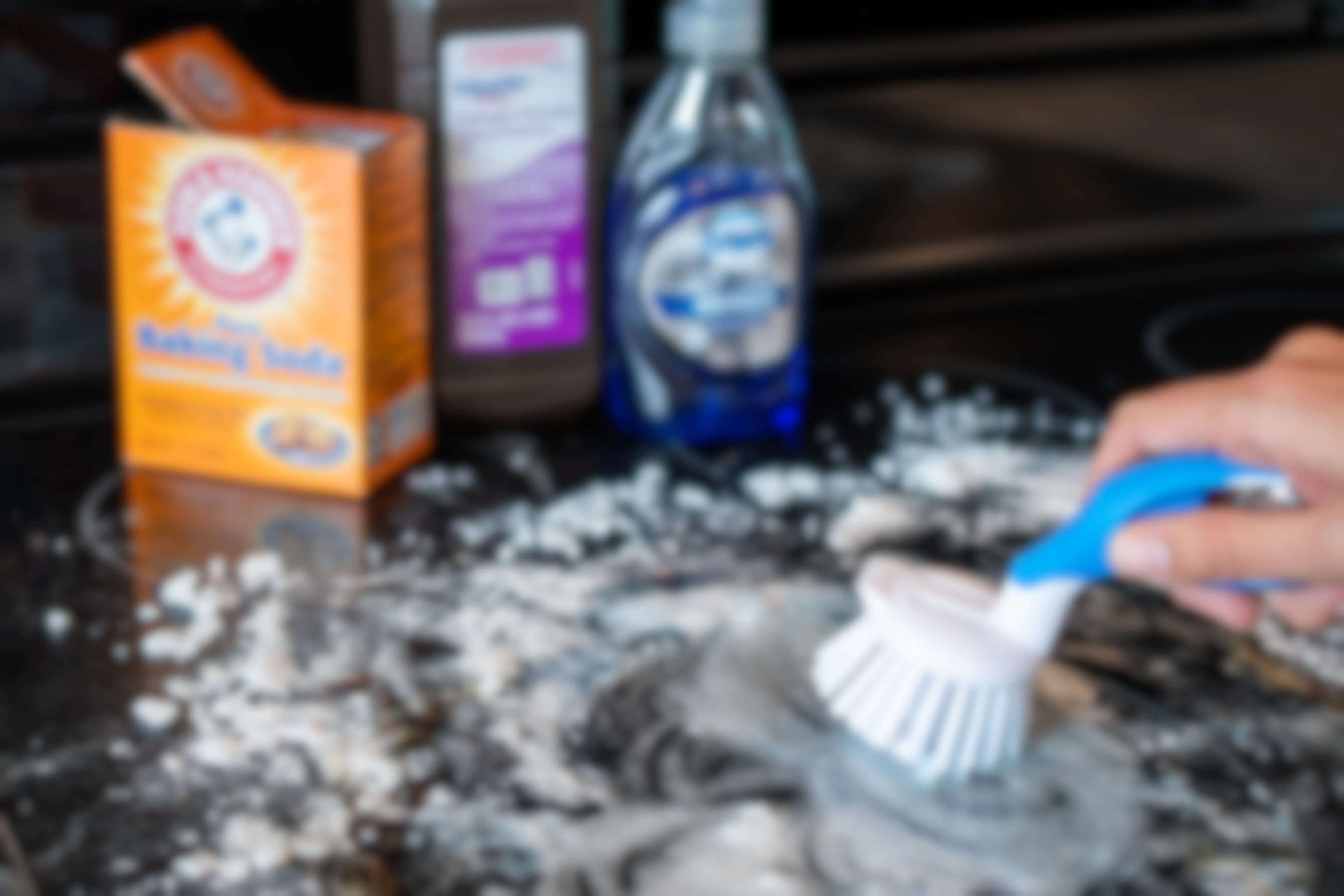 A person scrubbing a glass stove top with making soda, hydrogen peroxide, and dawn dish soap