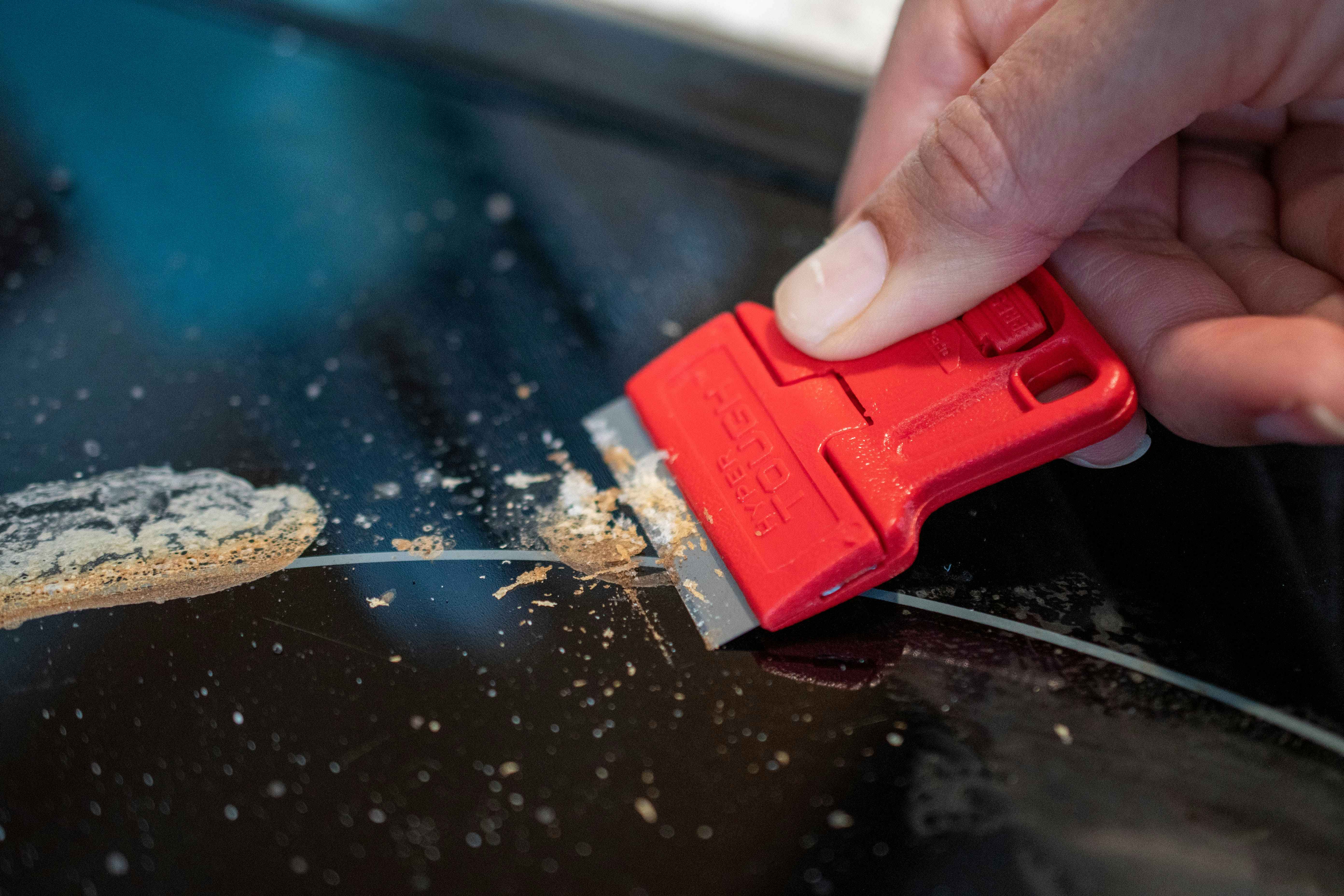 A person using a razor blade scraper to clean a glass cooktop stove