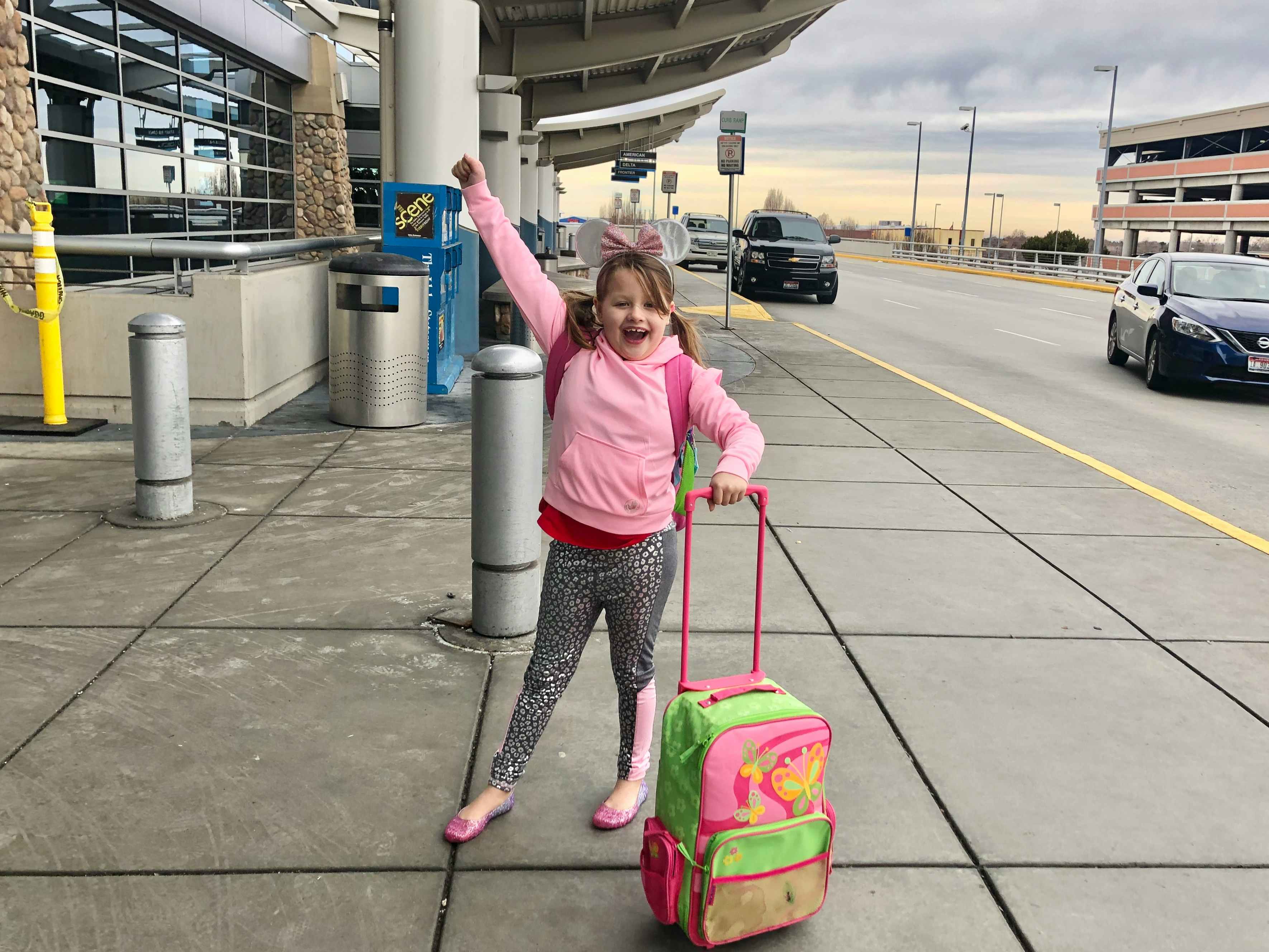 A little girl with Minnie Mouse ears walks in to an airport with her luggage.