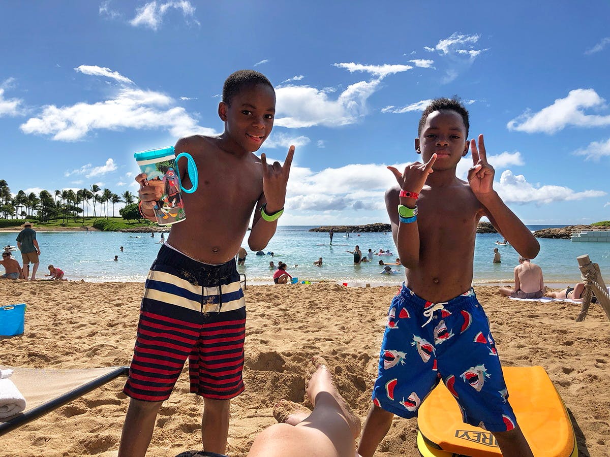 Two little boys holding Disney refillable cups on a beach.