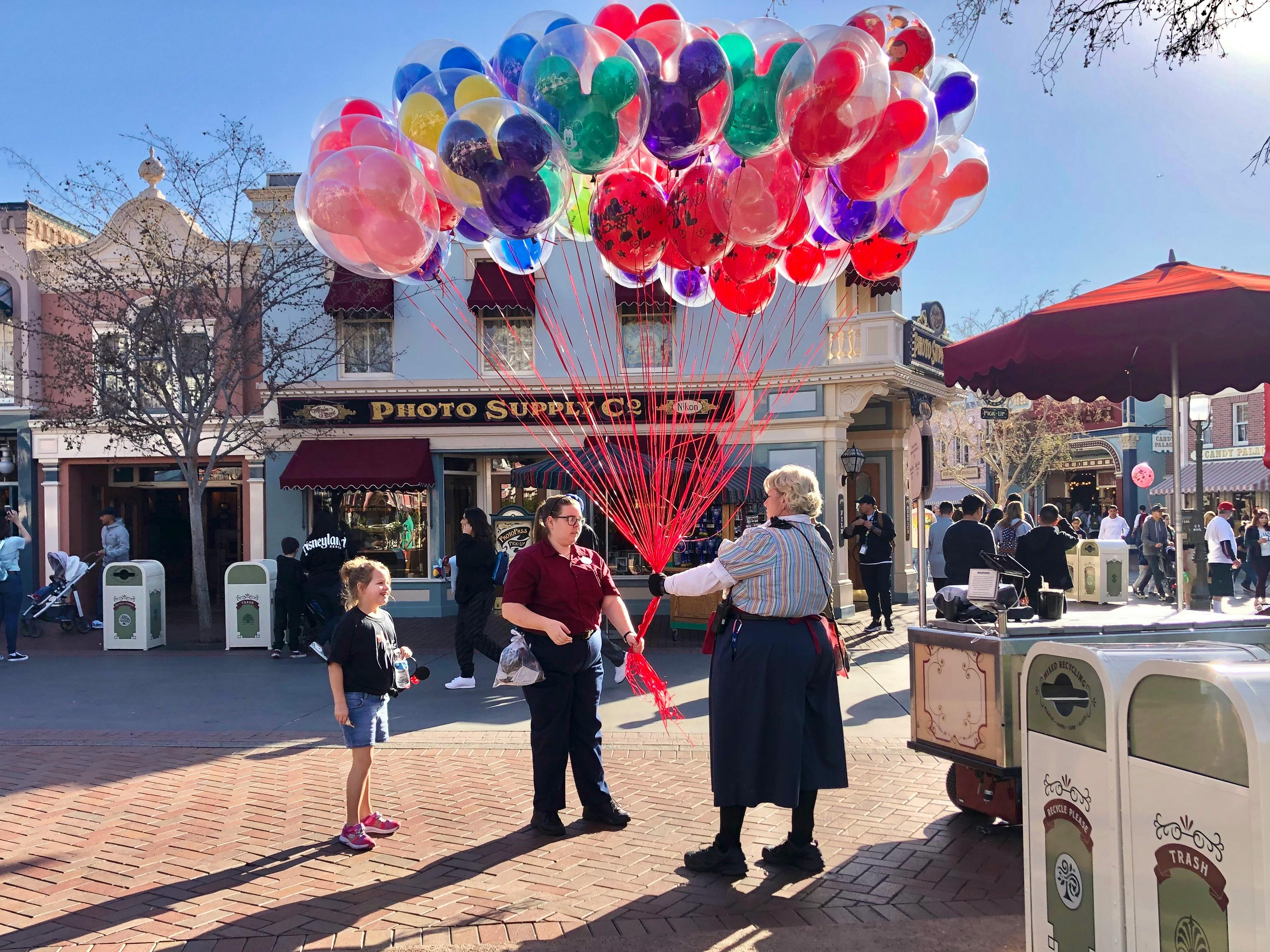 A little girl purchases balloons at Disneyland.