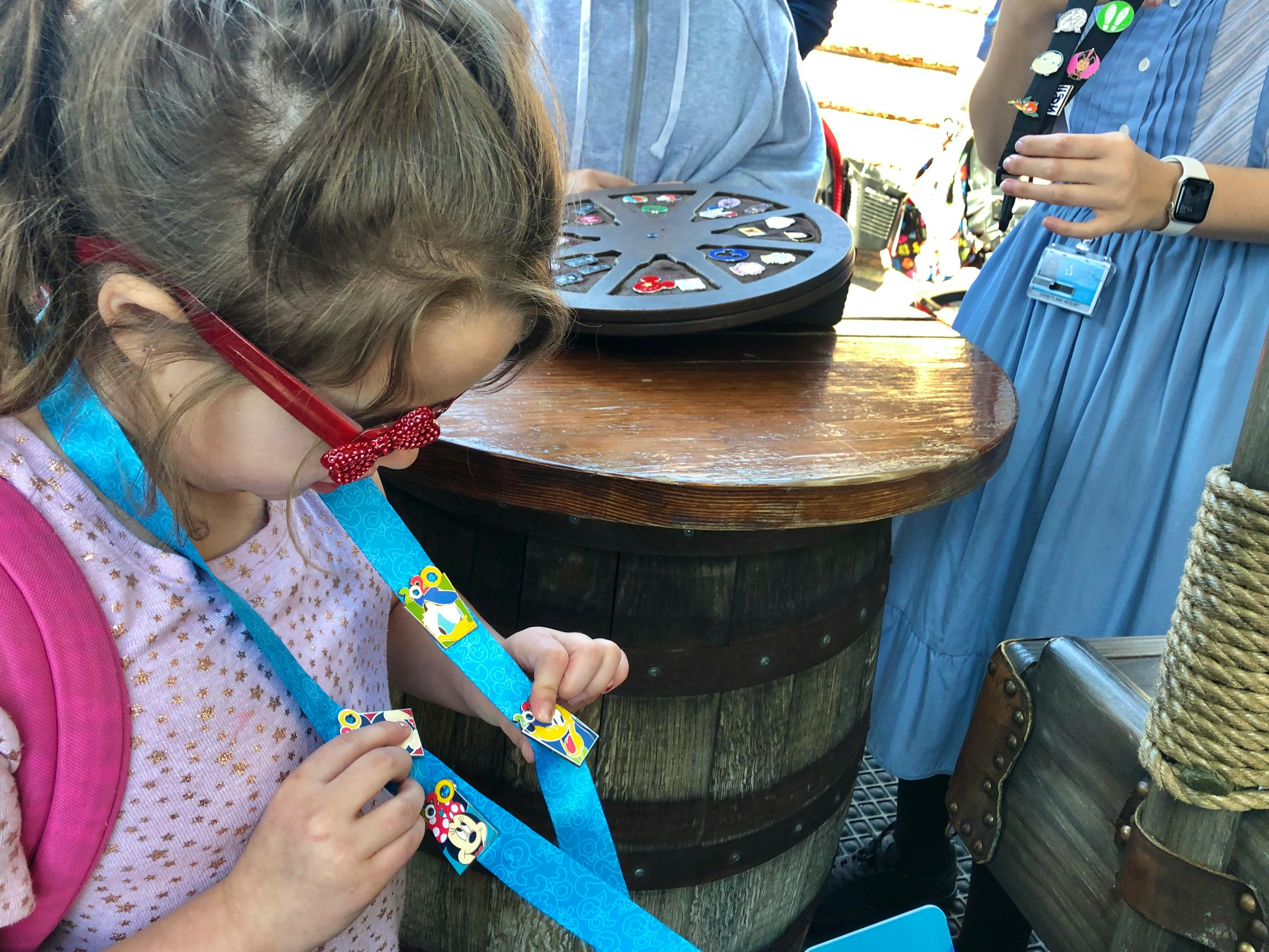 A child looking down at some Disney pins on a lanyard that she traded for at Disneyland.