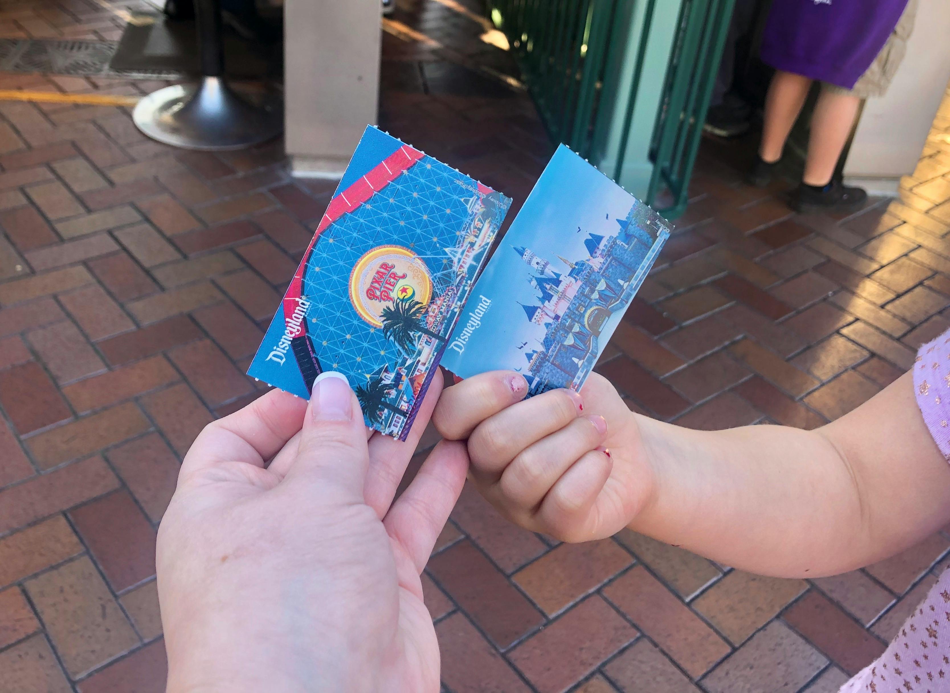 A mother and child hold up their tickets at Disneyland.
