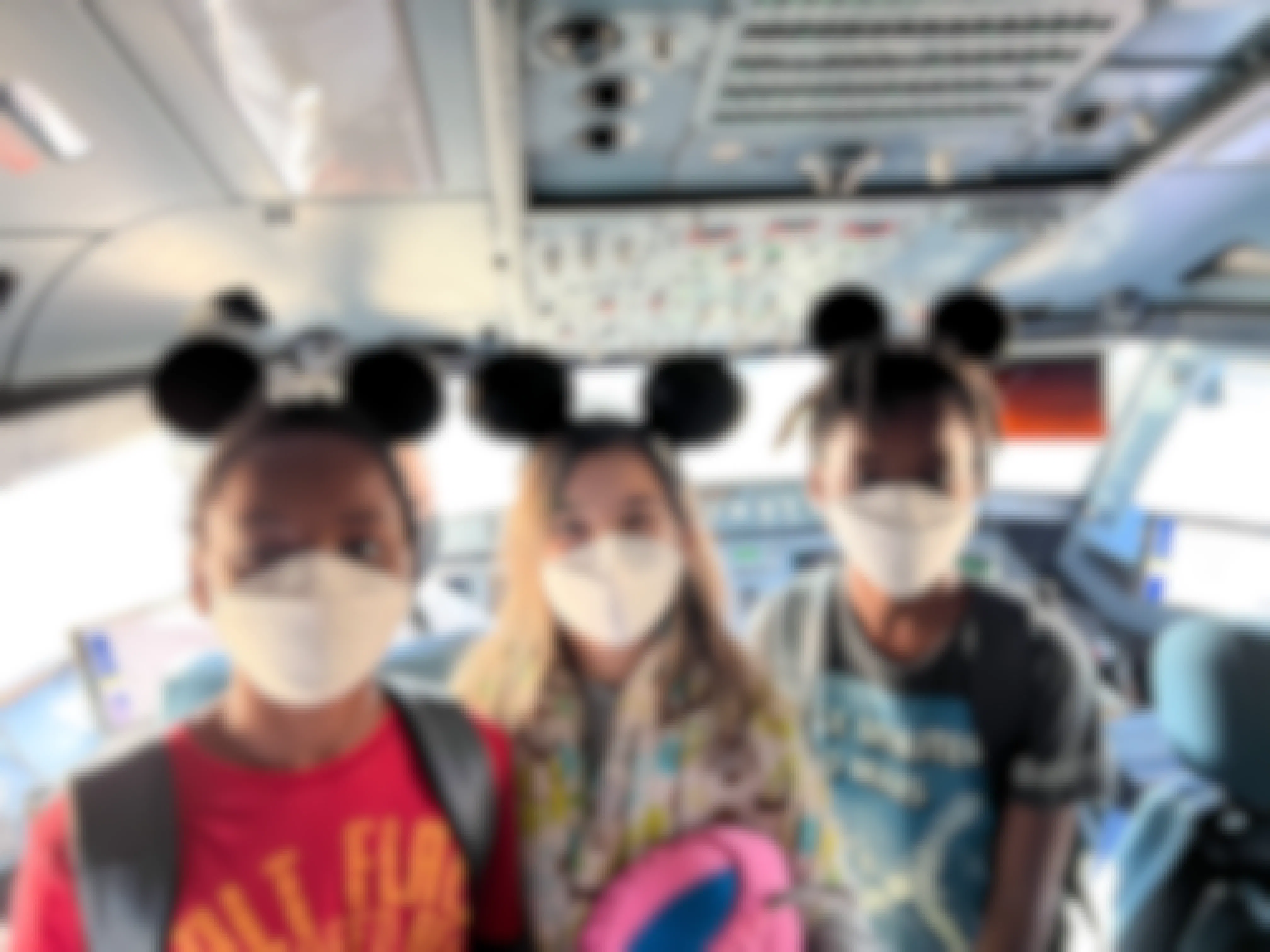 Three children with Mickey Mouse ears standing in the cockpit of a plane.