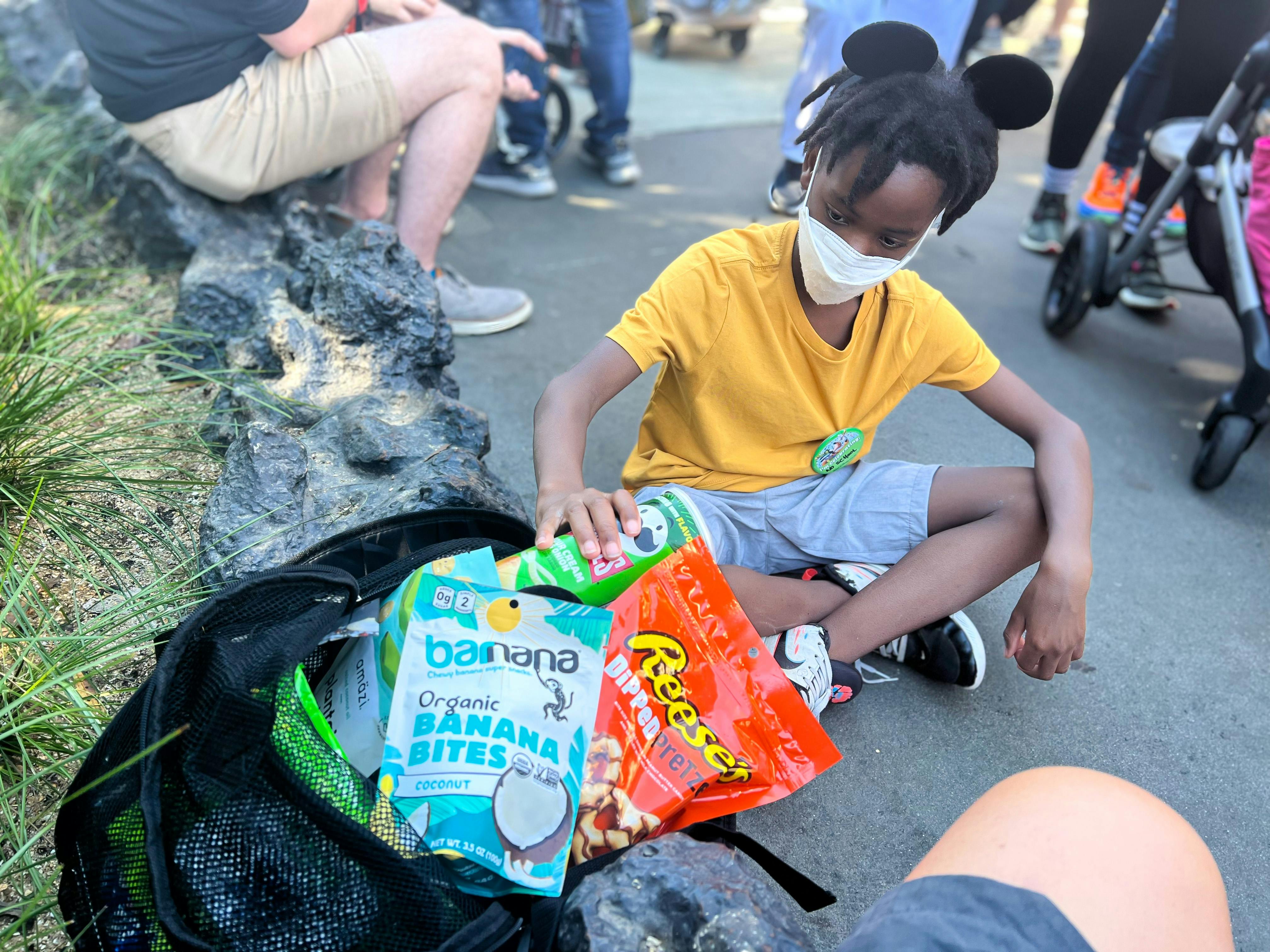 A kid with Mickey Mouse ears pulls snacks from a bag at Disney World