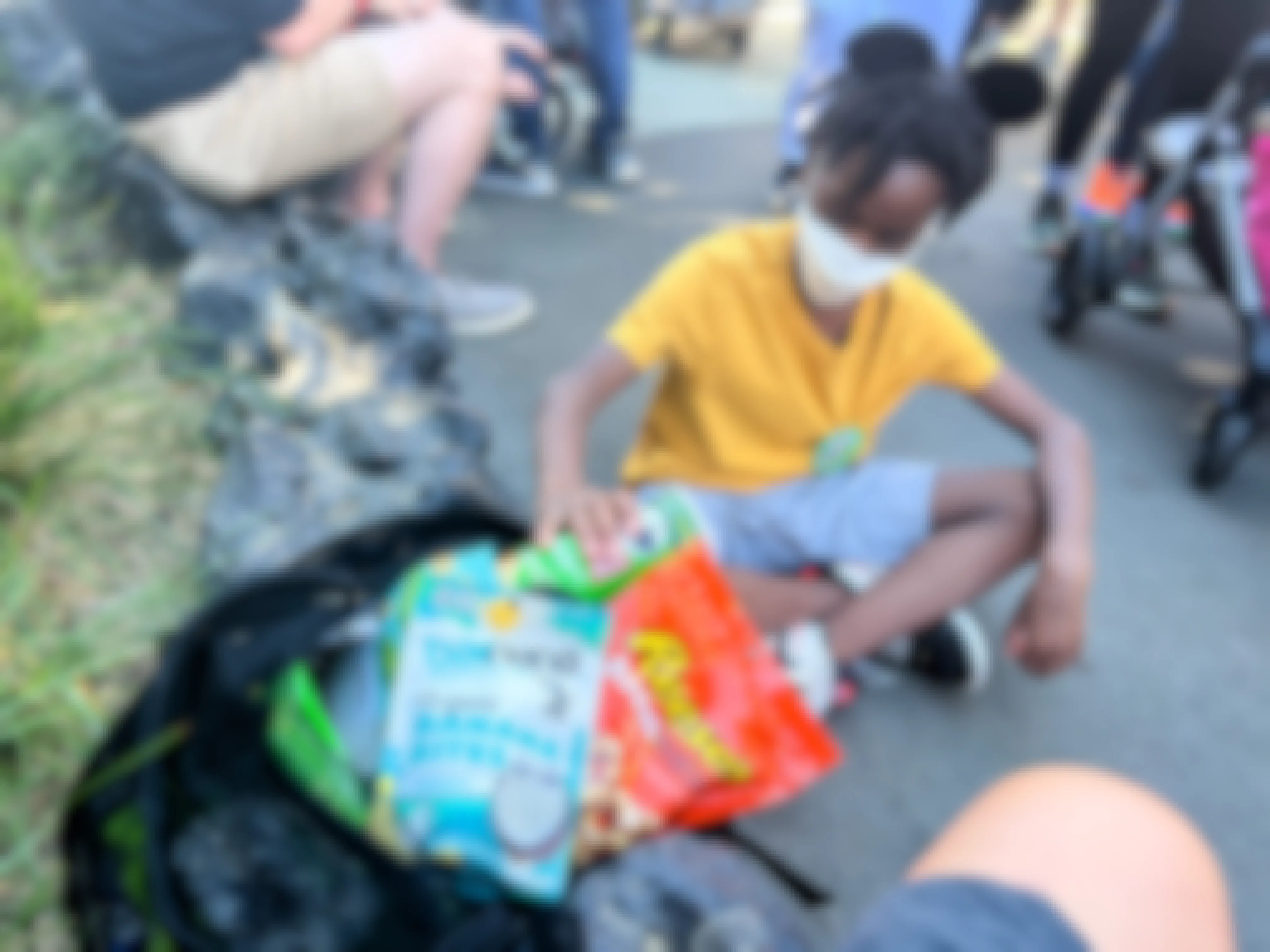 A kid with Mickey Mouse ears pulls snacks from a bag at Disney World