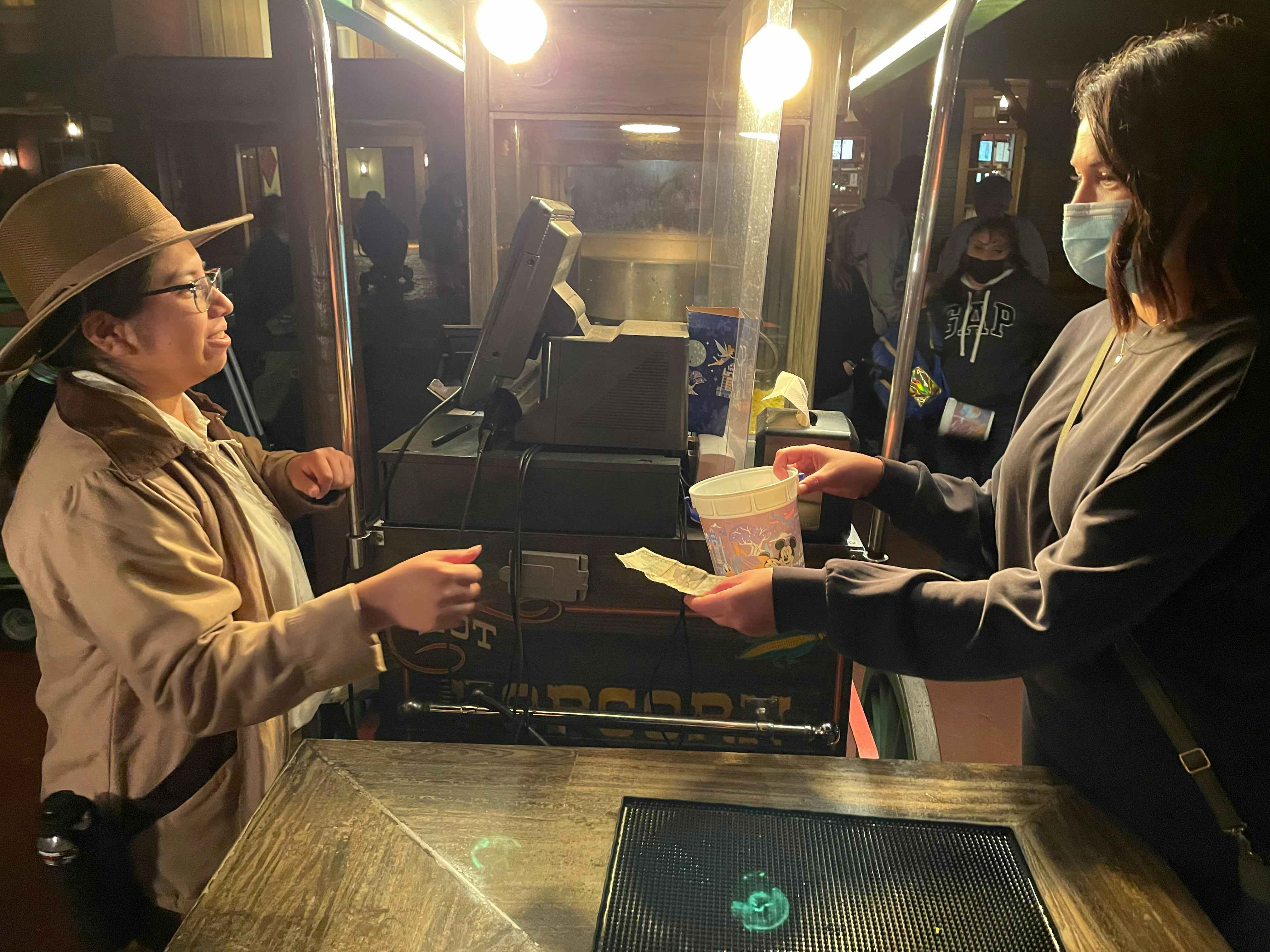 A person handing their souvenir popcorn container and a receipt to a Disney employee to get a $2 refill.