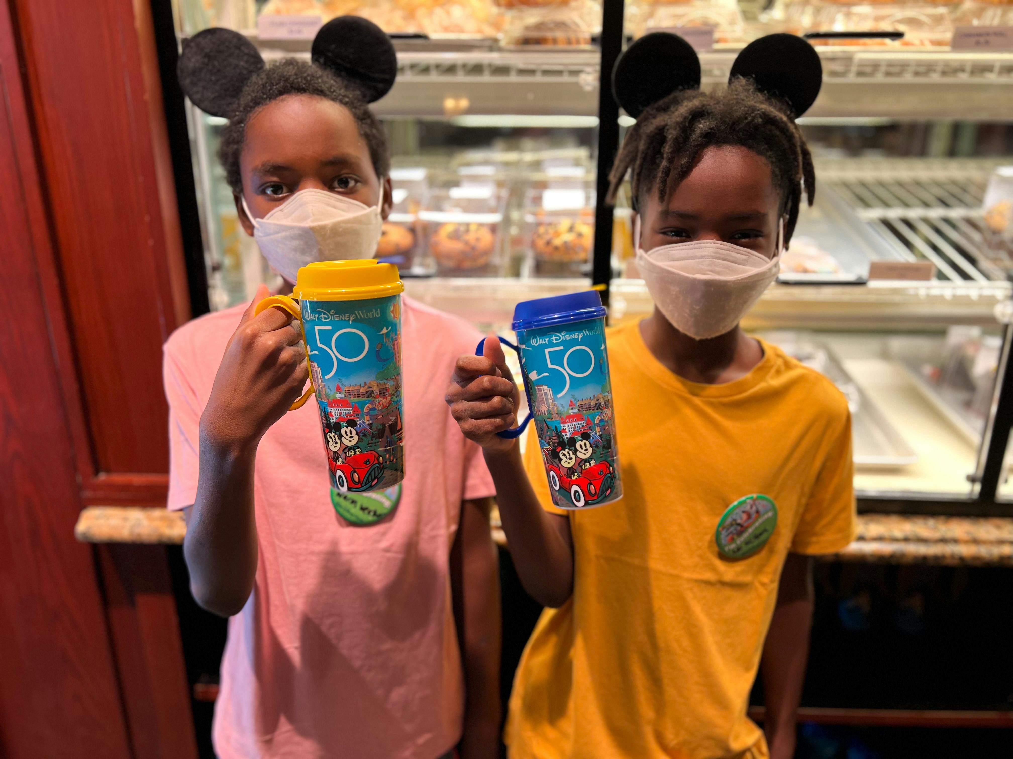 Two kids standing in front of a Disney restaurant holding reusable Disney drink cups.