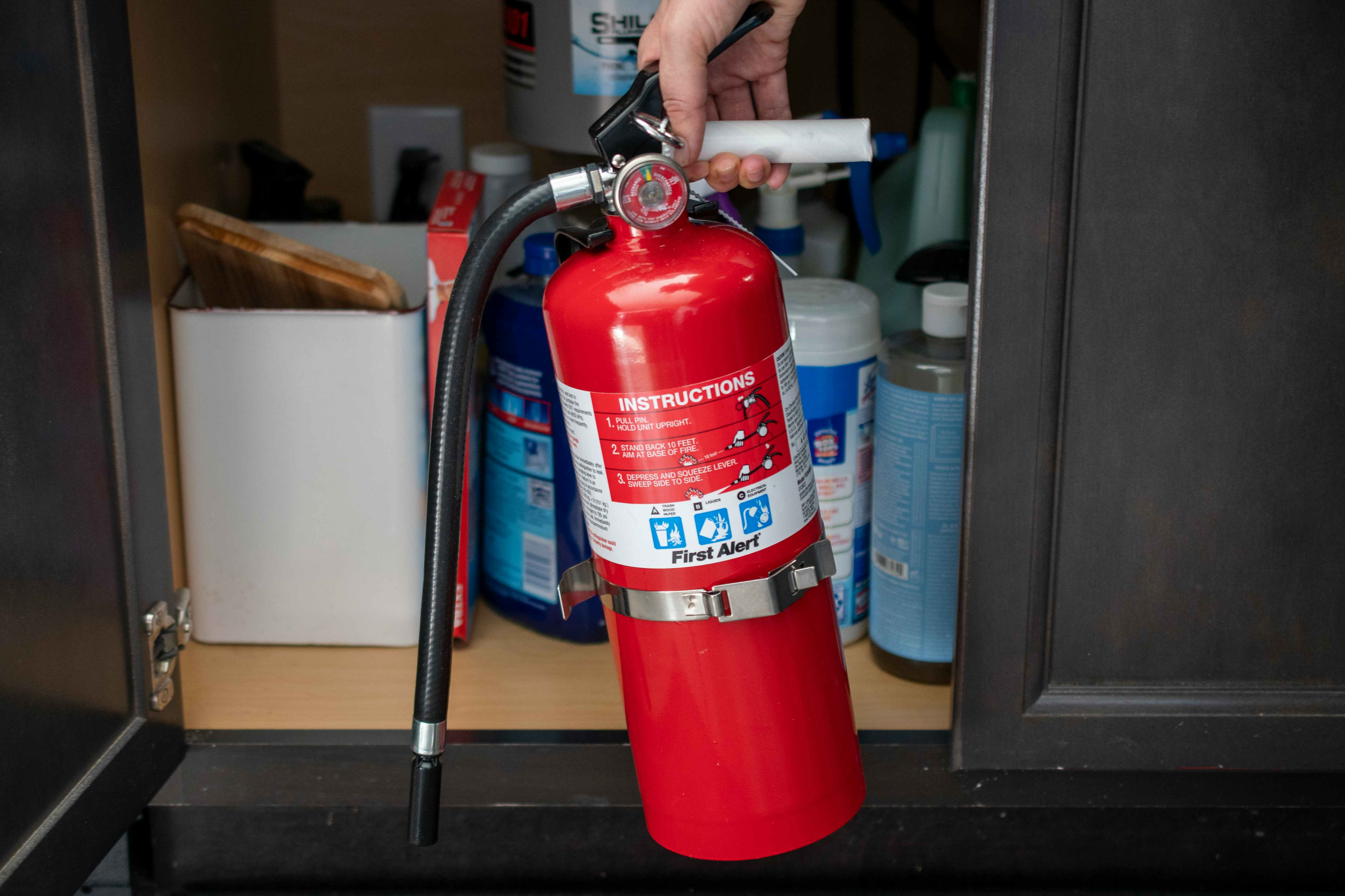 A person taking a fire extinguisher out from under a kitchen sink