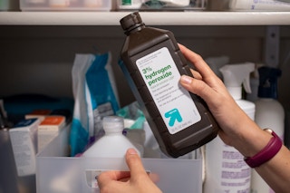 A woman pulling a bottle of hydrogen peroxide from a linen closet shelf