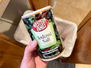 A canister of iodized salt held over a trash can
