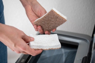 A person holding two kitchen sponges over a garbage can