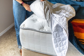 A person pulling back the sheets and mattress pad from a mattress