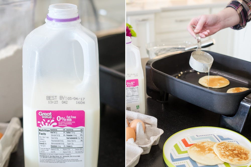 A jug of milk next to a person making pancakes on a griddle on a stove.