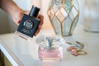 A woman holding a bottle of mens cologne next to a bottle of purfume