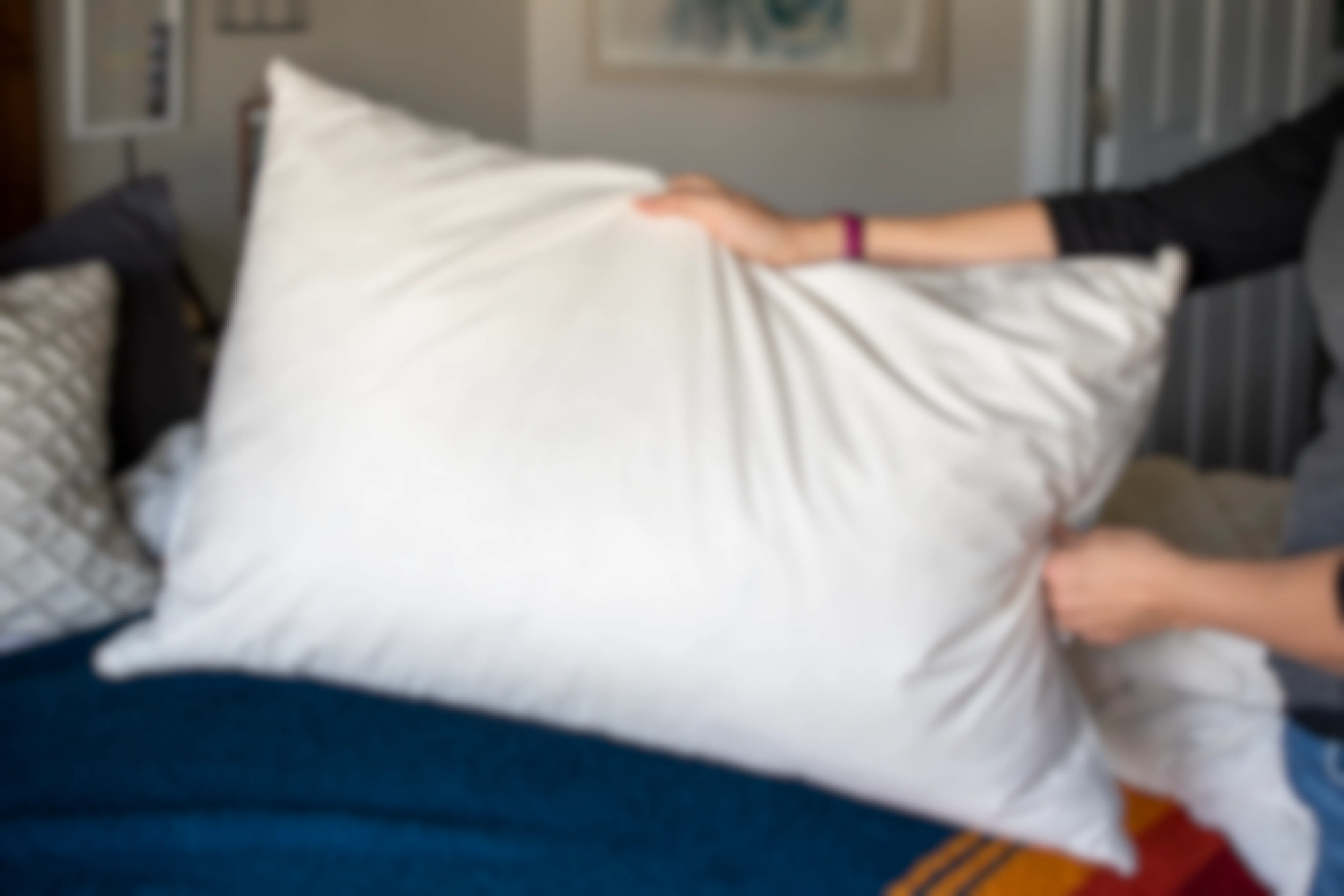 A woman holding a pillow with no pillow case over a bed.