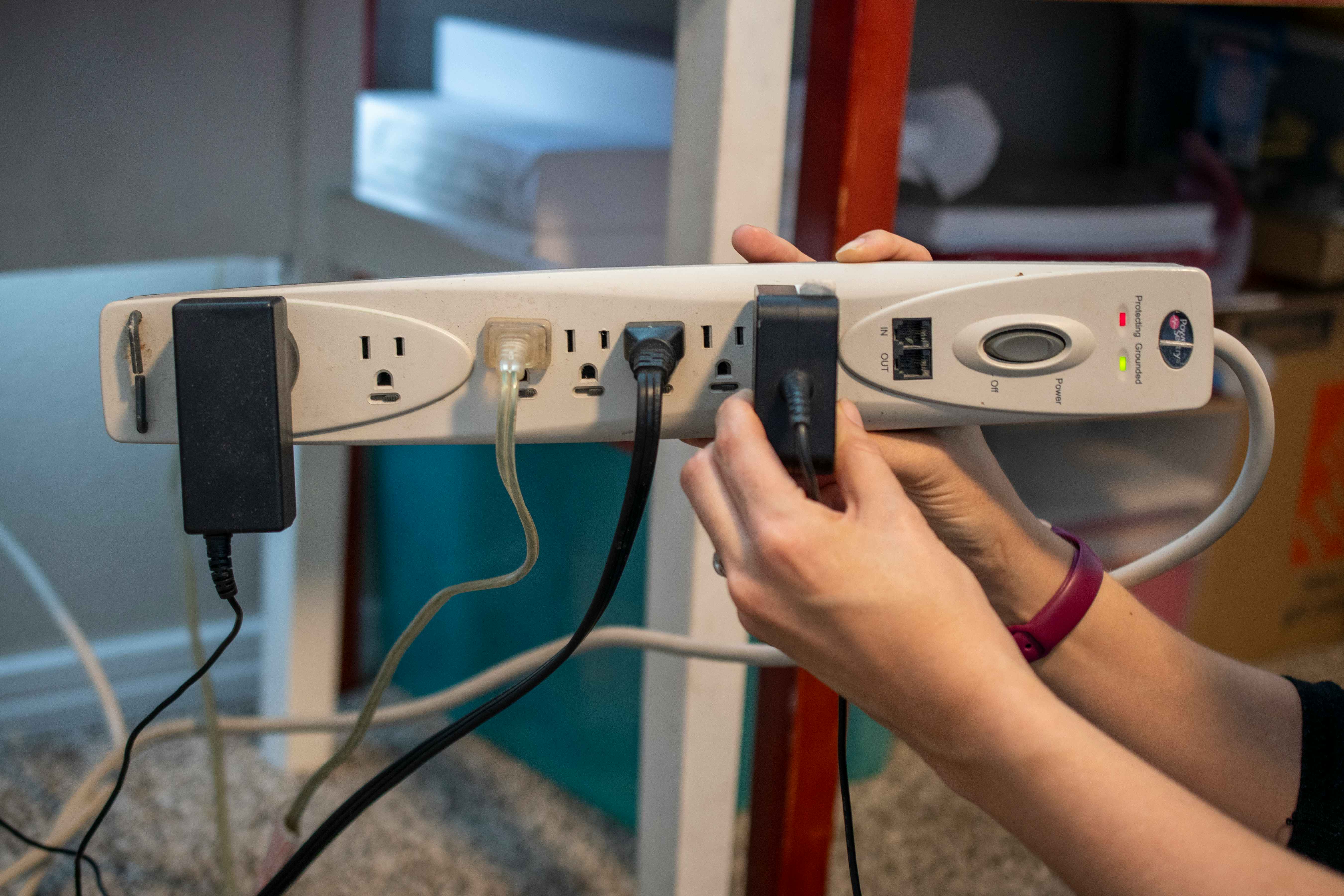 A woman holding up a power strip with a bunch of cords plugged into it.