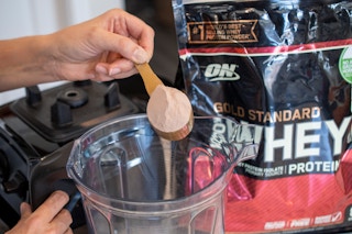 A woman pouring protein powder into a blender.