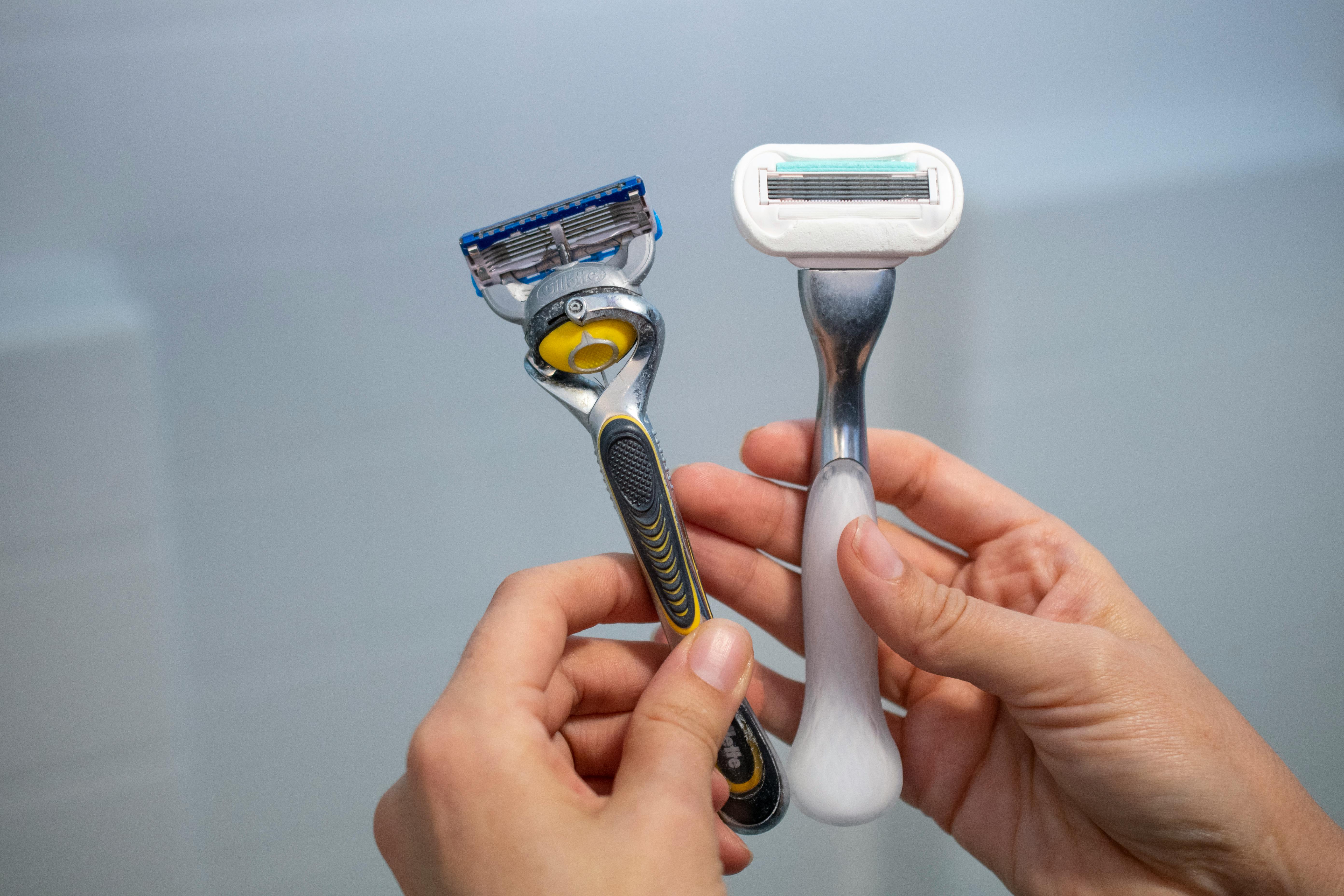 A woman holding a two razors next to a shower