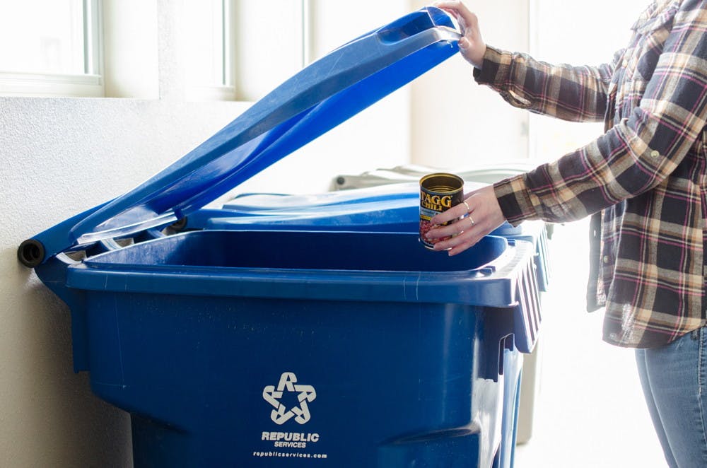 A person putting an empty food can into a recycling bin.