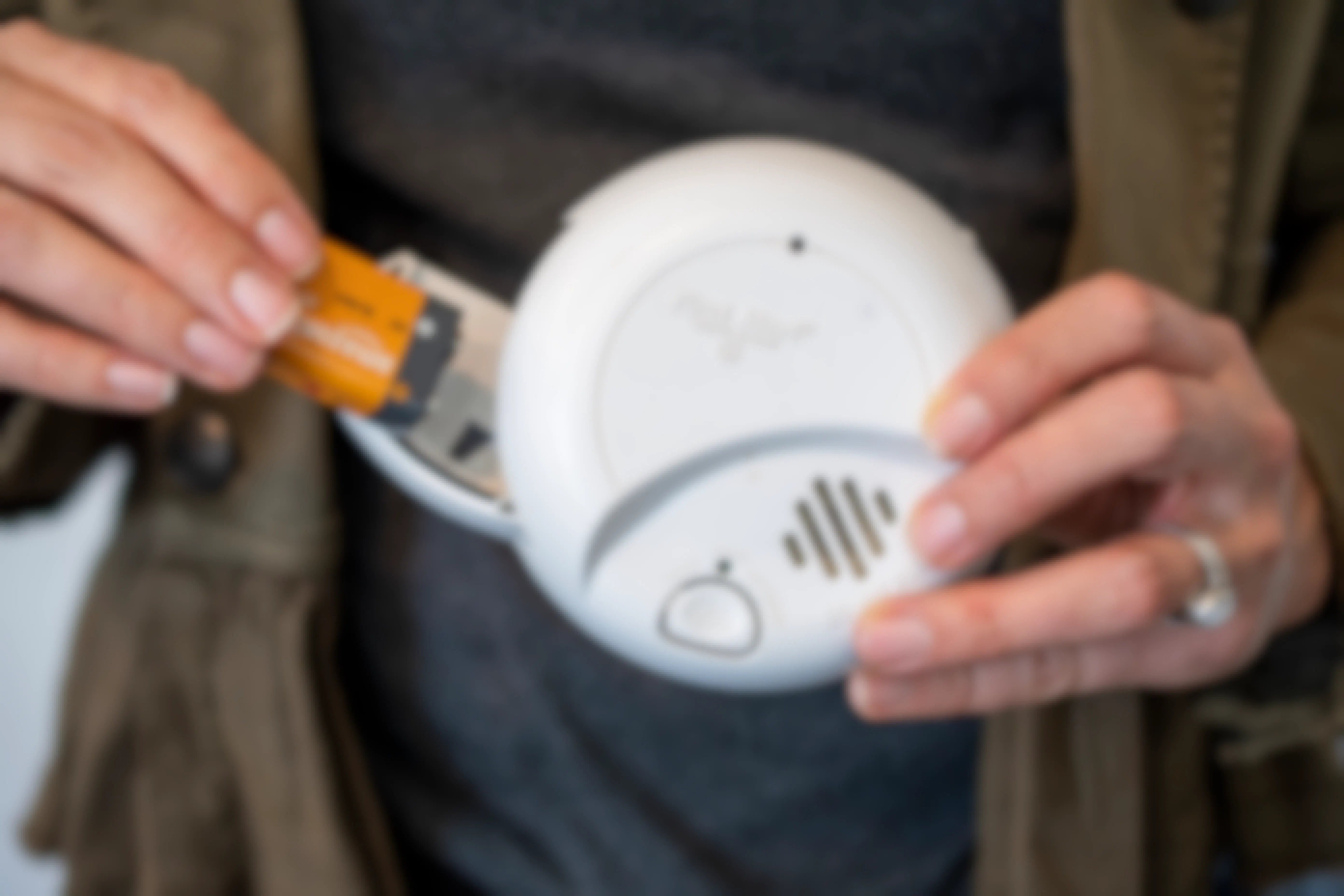 A person holding batteries and a smoke alarm.