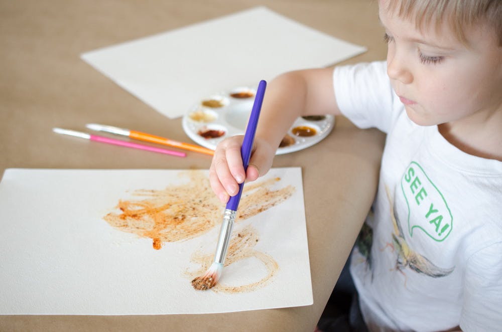 A child painting on a piece of paper with paints made from spices.