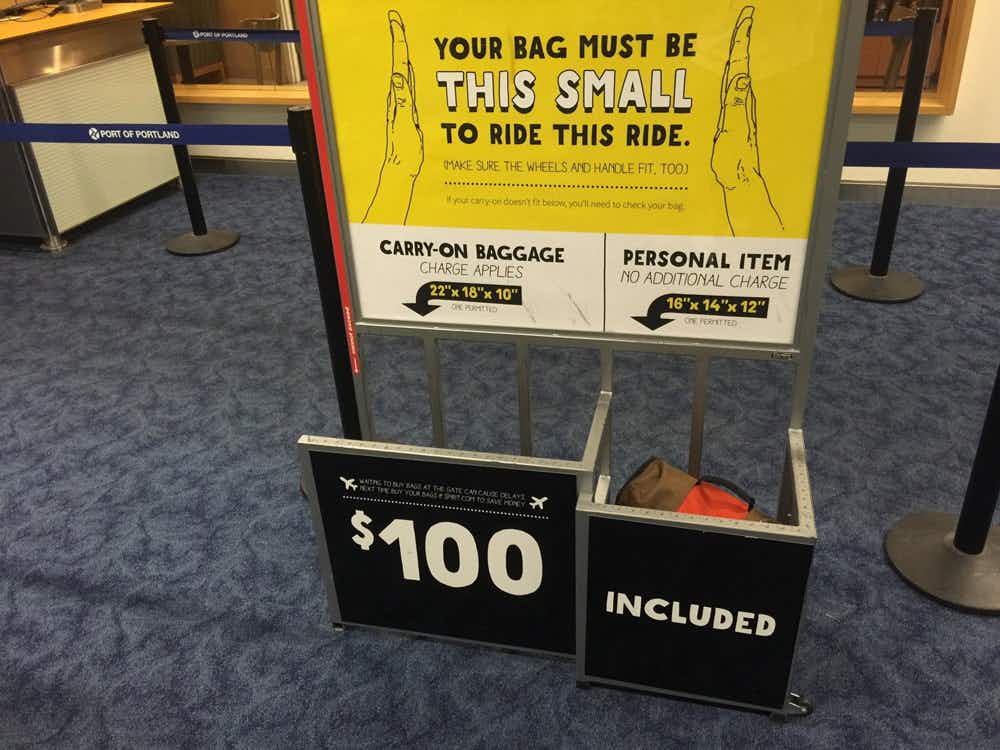a Spirit airlines sign for baggage with a sign that says $100 if your bag doesn't fit the requirements