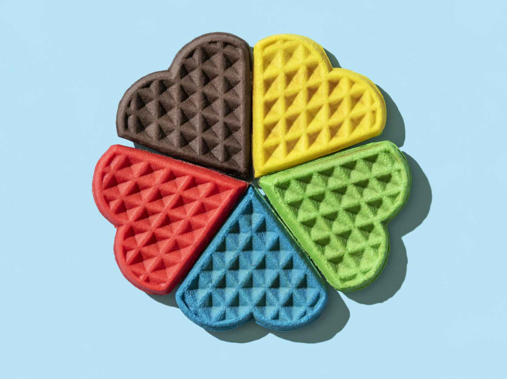 Rainbow colored heart-shaped waffles arranged on a blue background
