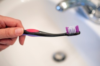 Person holding a toothbrush over a sink