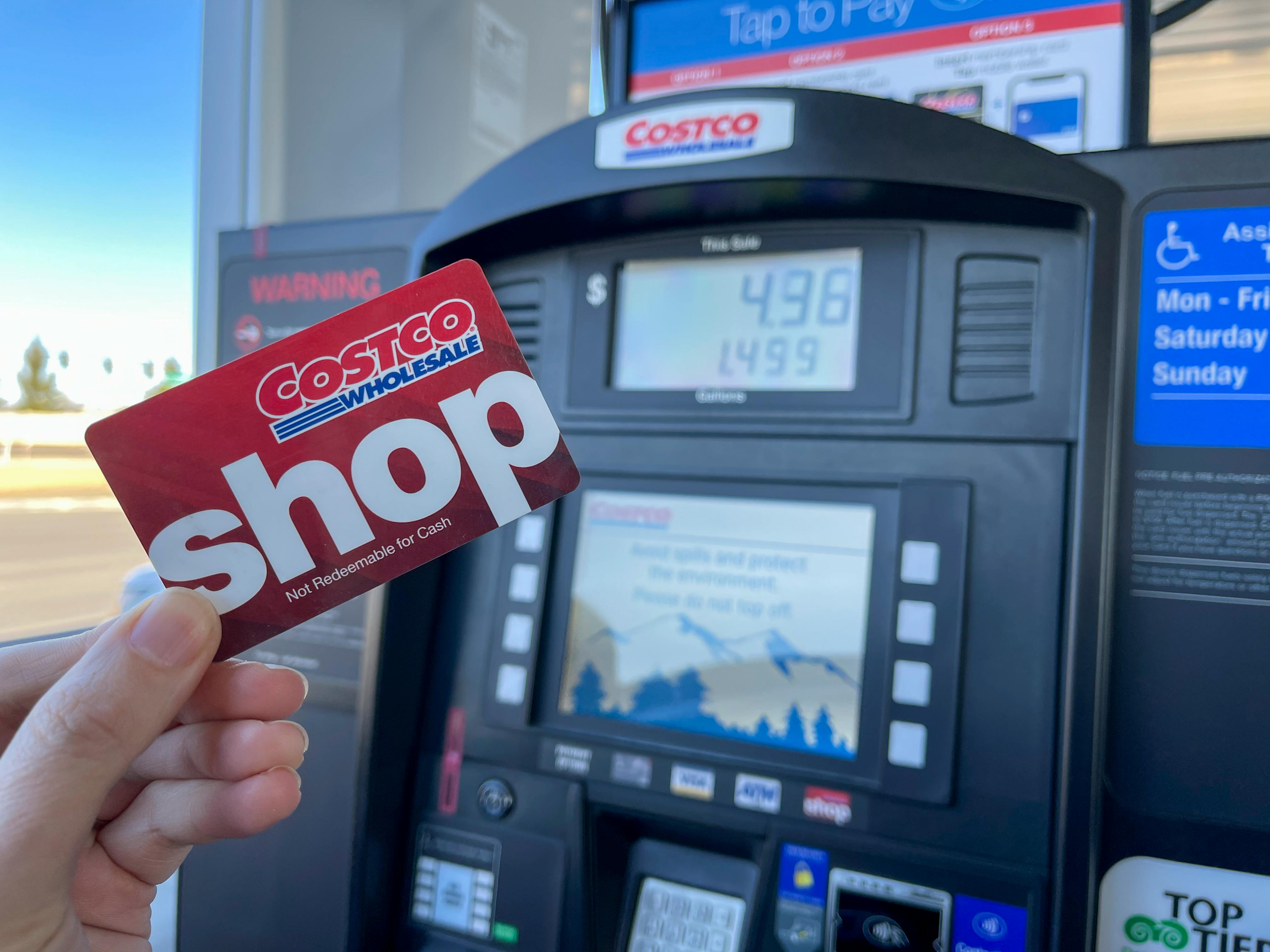 A person holding a Costco wholesale shop card in front of a gas pump