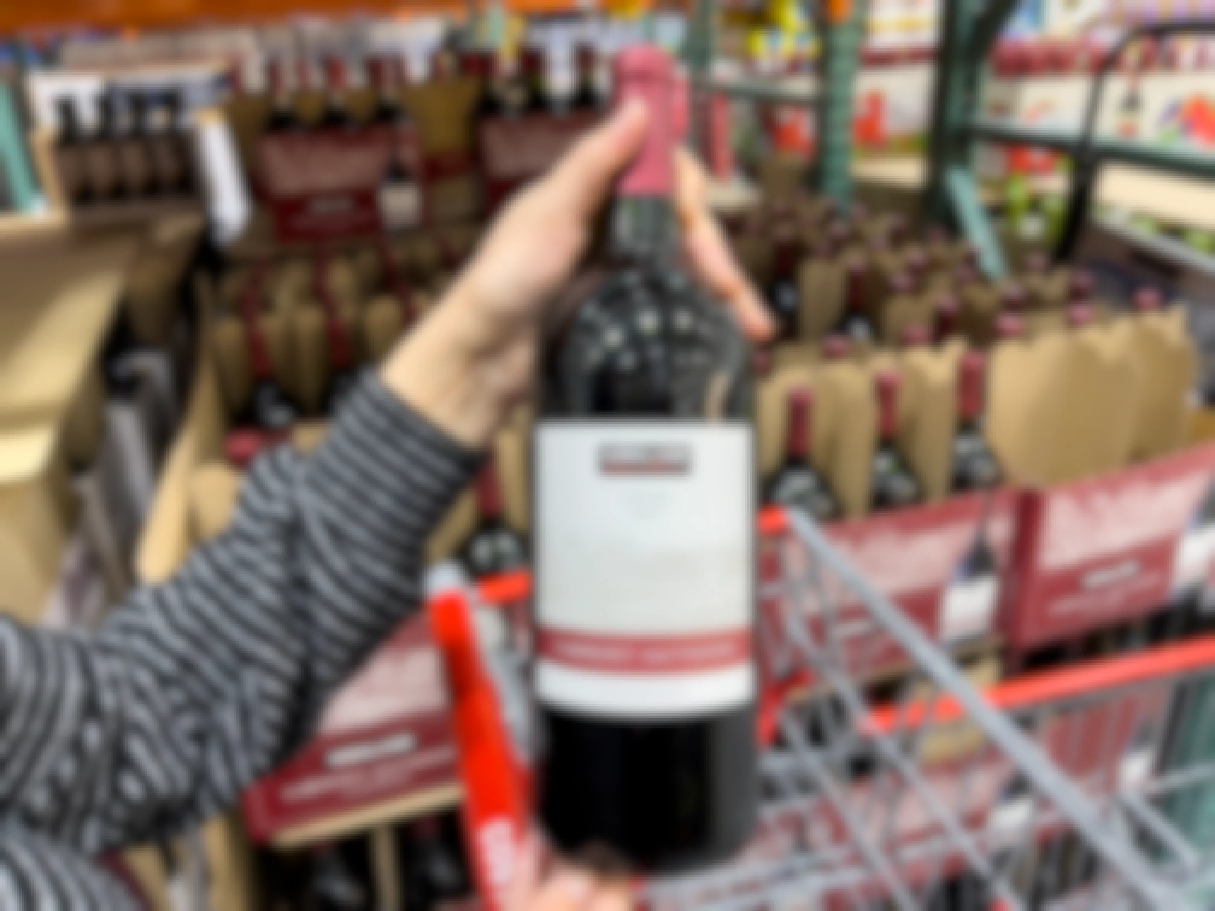 A person holding a bottle of Kirkland brand Cabernet wine over a shopping cart.