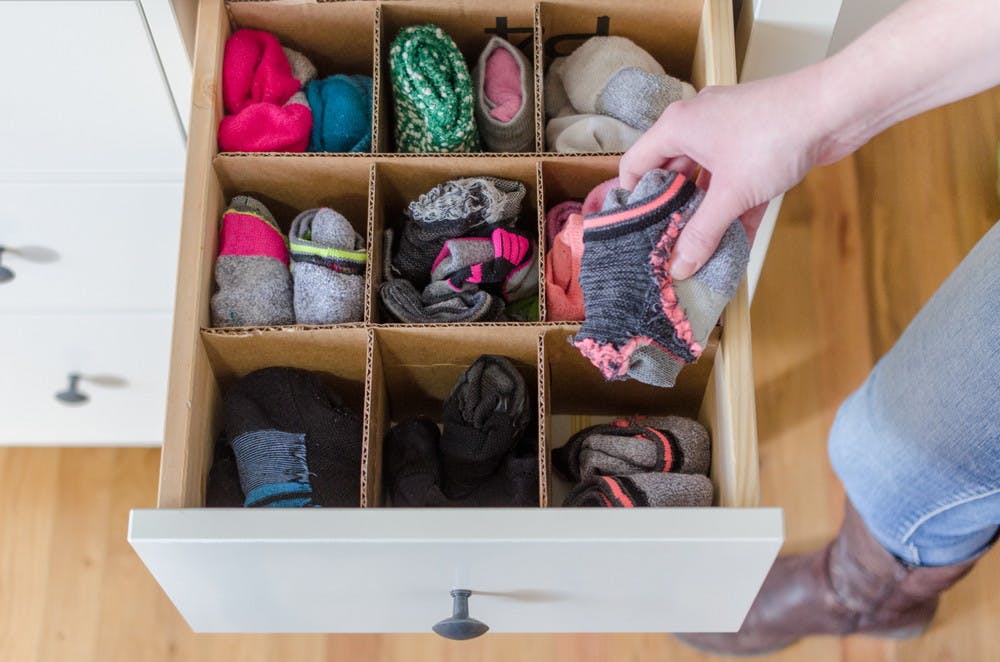 Someone using a cardboard box as drawer dividers for socks