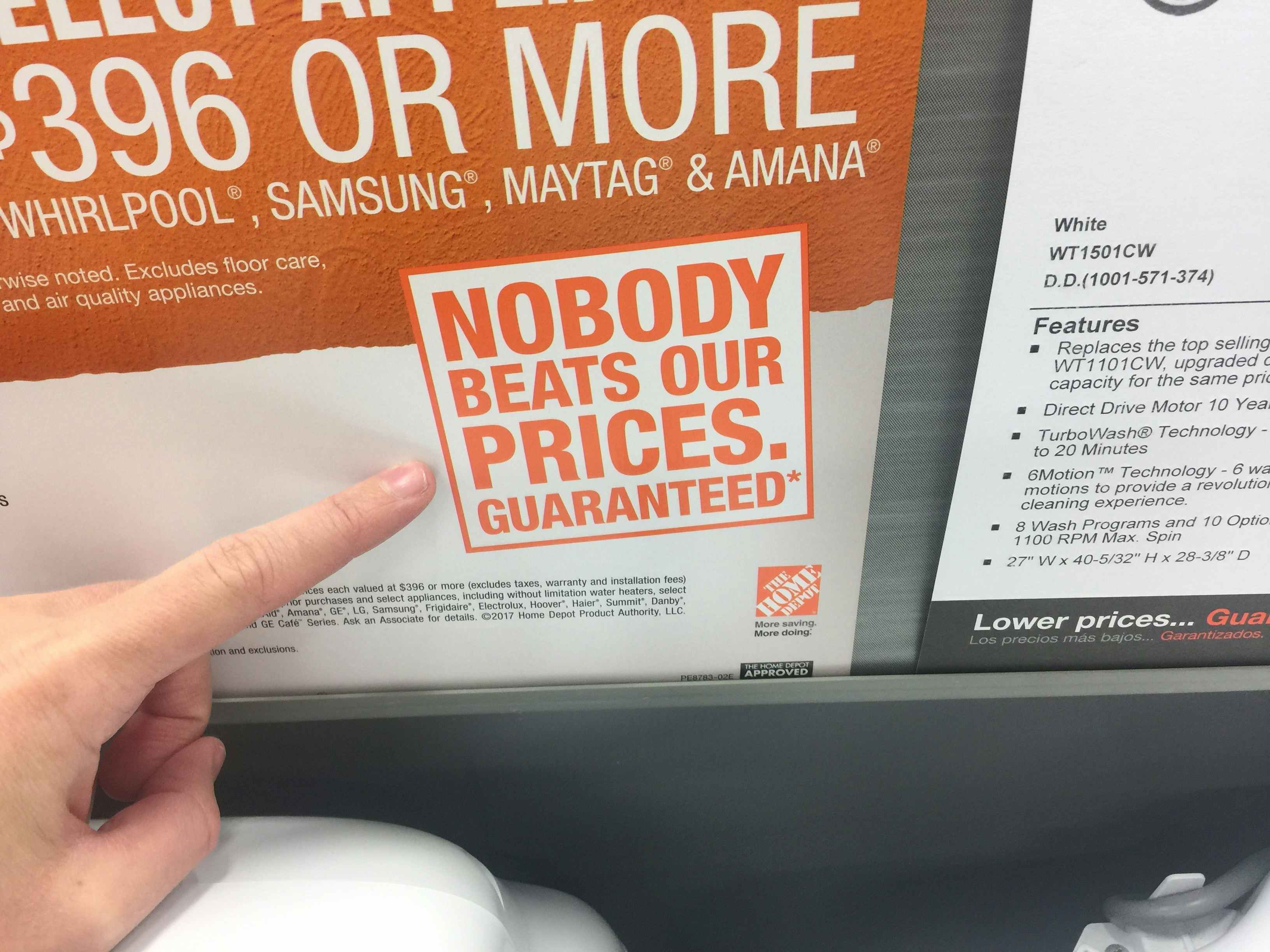 A person pointing to the graphic that reads, "Nobody beats our prices. Guaranteed*" next to the Home Depot price match policy on the wall inside Home Depot.