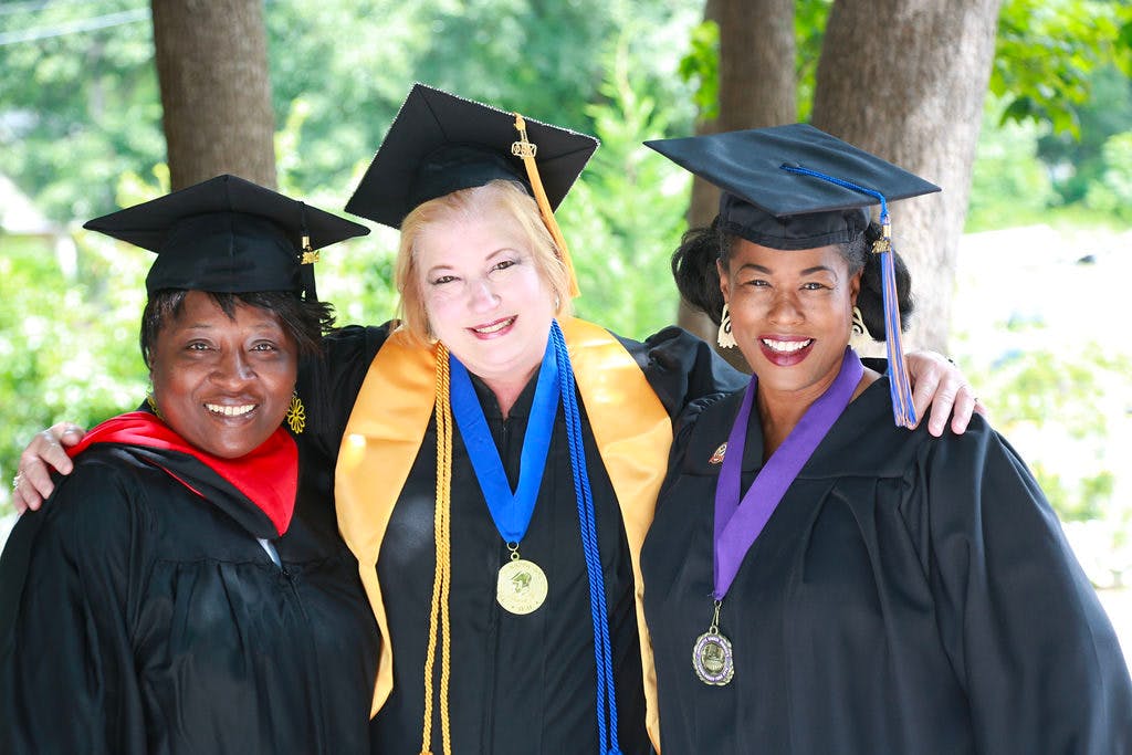 Three women posing and smiling for the camera while wearing graduation caps and gowns.