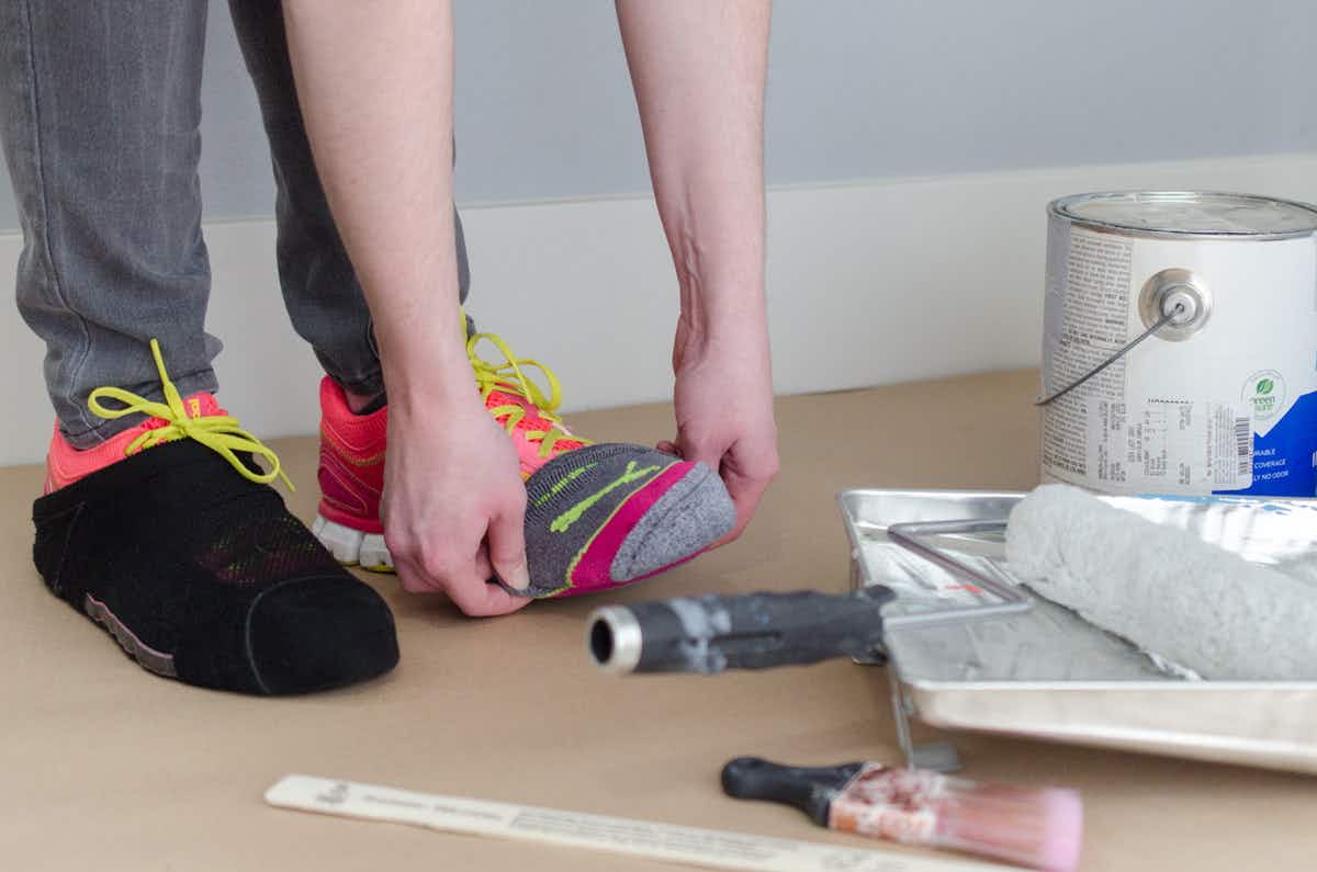A person putting a sock on over their shoe to prevent paint stains when painting.