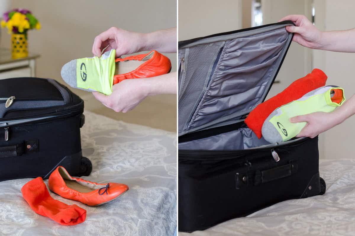 A person putting shoes inside socks next to a suitcase.