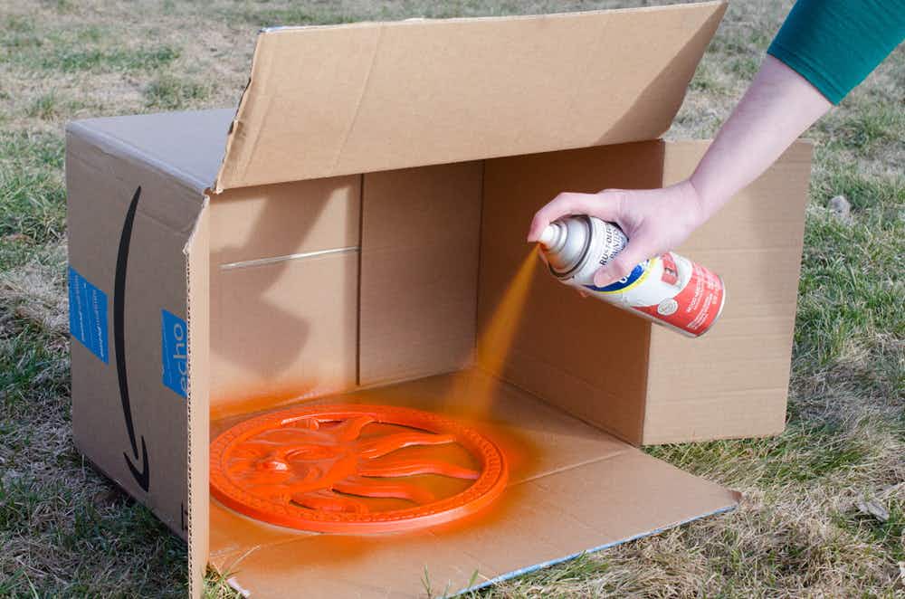 A person spray painting a flat object inside a cardboard box.