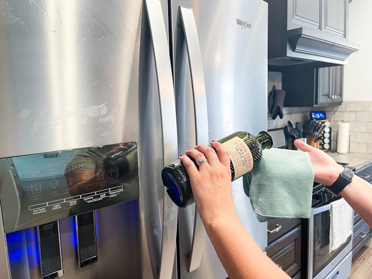 person pouring olive oil on cloth to clean fridge