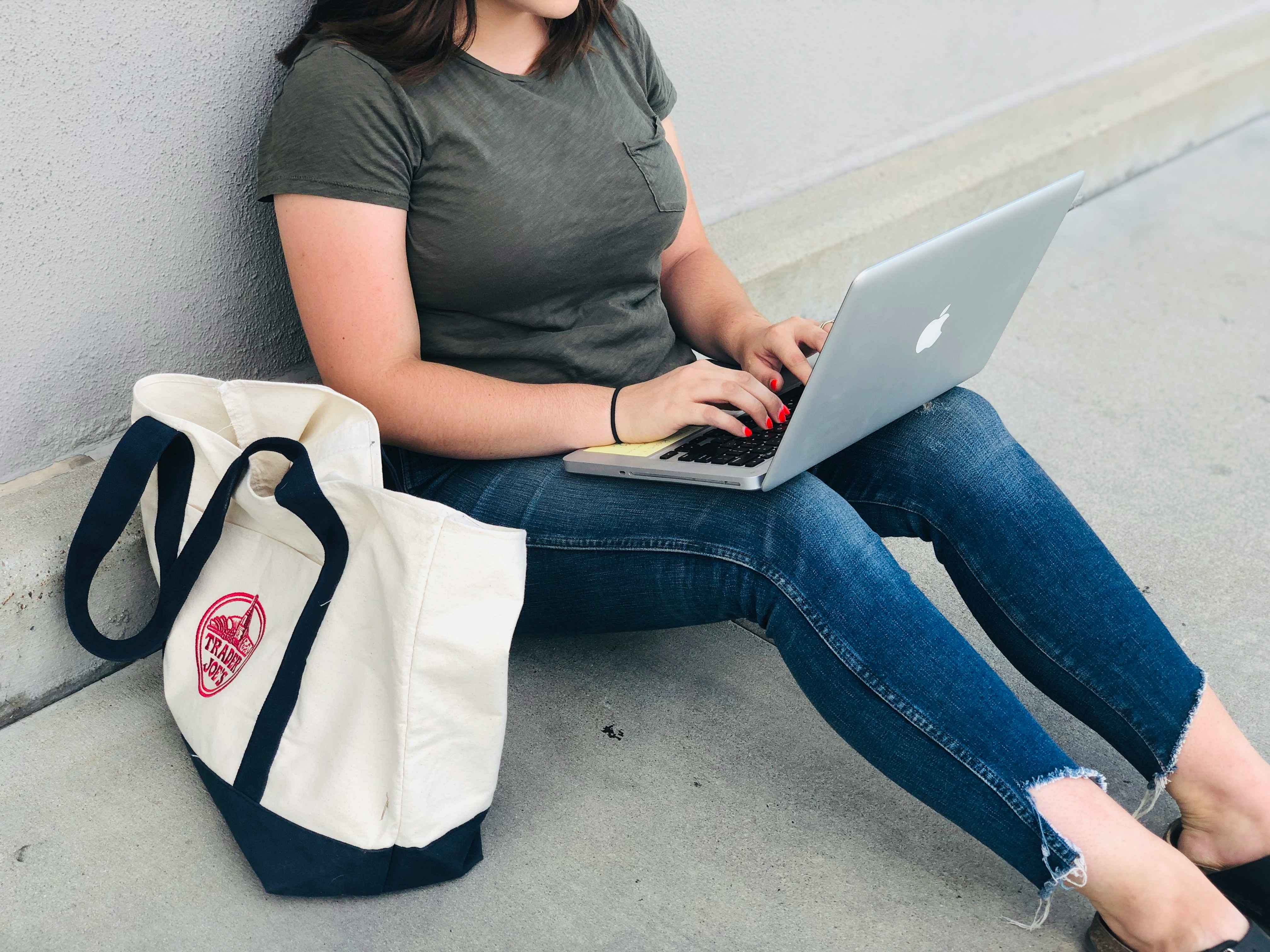 A student sitting against a wall typing on a laptop