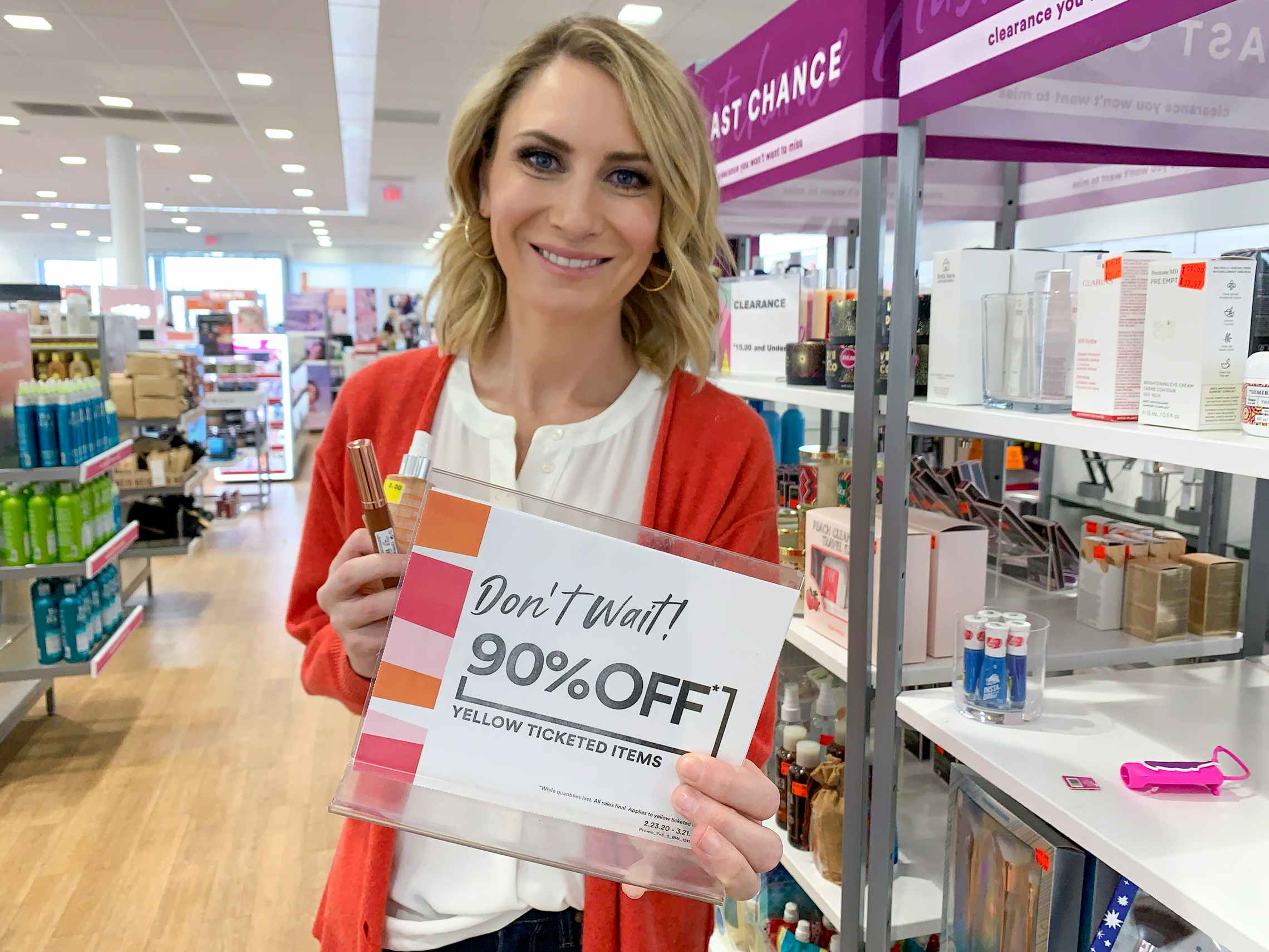 A woman holding up a sign in front of a clearance shelf that says "Don't Wait! 90% Off