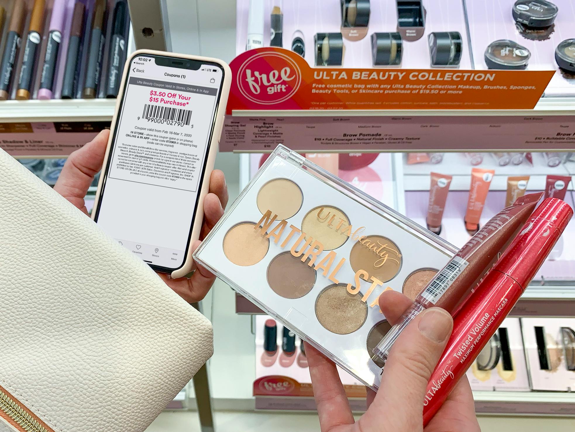 A person holding a cell phone displaying an Ulta coupon in one hand with a free gift makeup bag and Ulta Beauty cosmetics in the other hand.